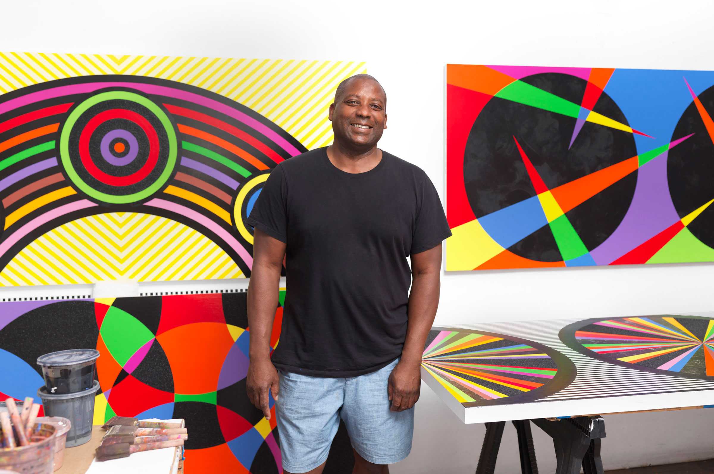Man standing in front of colorful geometric paintings in an art studio.