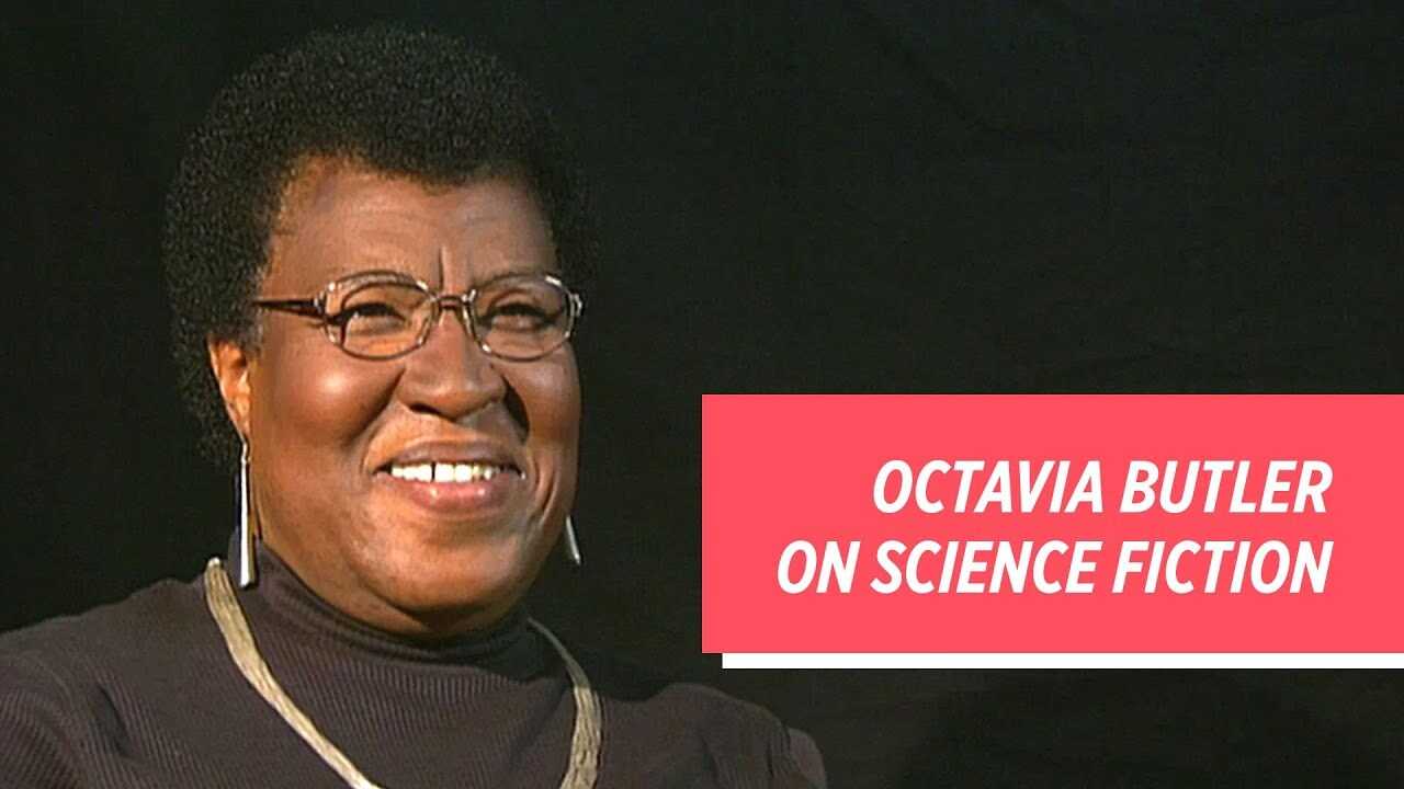 Octavia Butler smiling wearing a black turtleneck and a chunky gold necklace against a black background