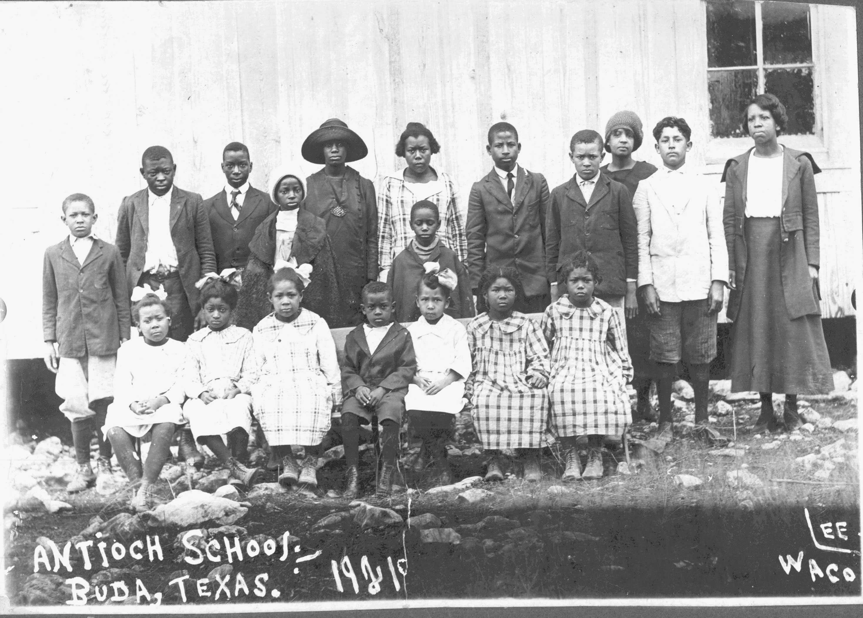 Students pose for a class photo in front of their school. Students age range from young children to teenagers.