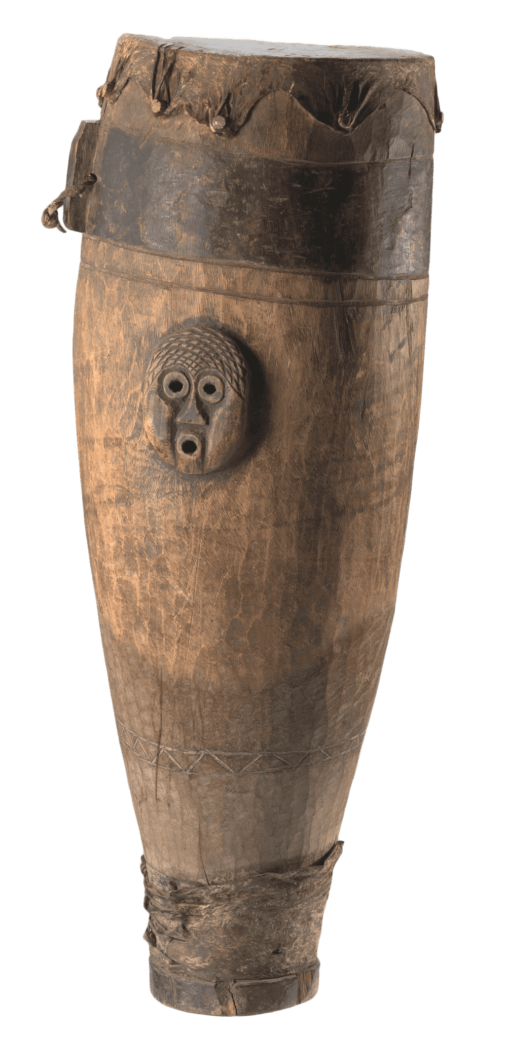 A wooden drum covered with stretched leather hide that has been attached to drum body with nine wooden pegs. Two carved, anthropomorphized face motifs are on opposite sides of the upper half of the drum body. The edges of face motifs have been sealed with a darker adhesive material. There are three bands running the circumference of the drum. The top band closest to the drum head, is stained darker than the rest of the drum body. There is a carved piece that extends from the darker band. It has a round drill hole  that had been threaded through with a leather thong. This piece has been stained the same color as the bank. The middle band is directly below the top band and above the face motifs. It is the same color as the rest of the body. The bottom band is a carved triangular pattern between two parallel lines. The bottom band is located near the base of the drum, above a piece of hide wrapped and tied around the very bottom of the drum body. There is a nail visible in drum body interior.
