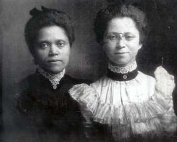 Black-and-white historical photograph of two women standing side by side, dressed in formal late 19th or early 20th-century attire.