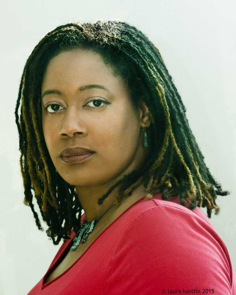 An author photo of N.K. Jemisin. She is wearing a long red sleve shirt, looking directly at the camera.