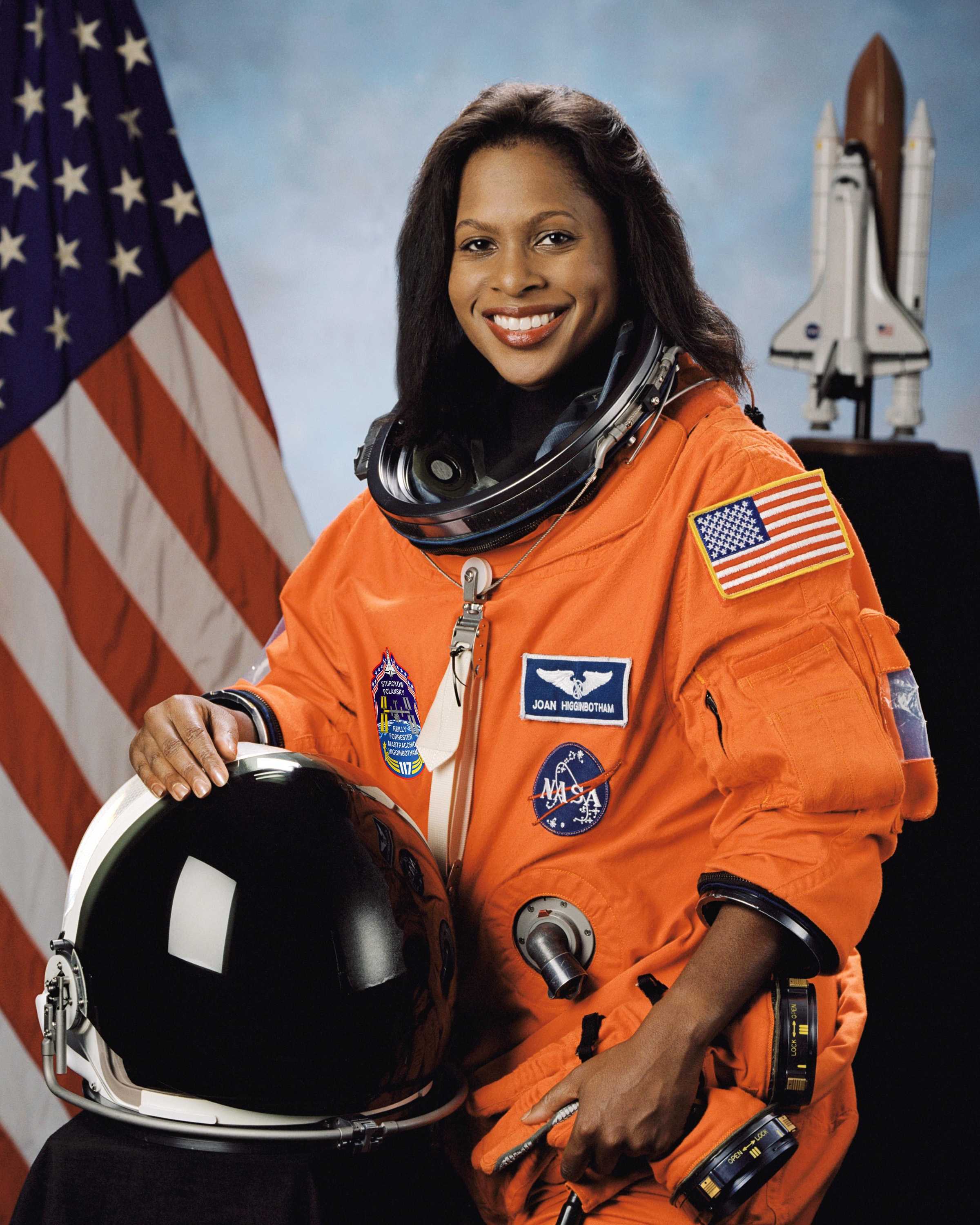 Joan Higginbotham smiles for her portrait while holding a helmet in front of her.