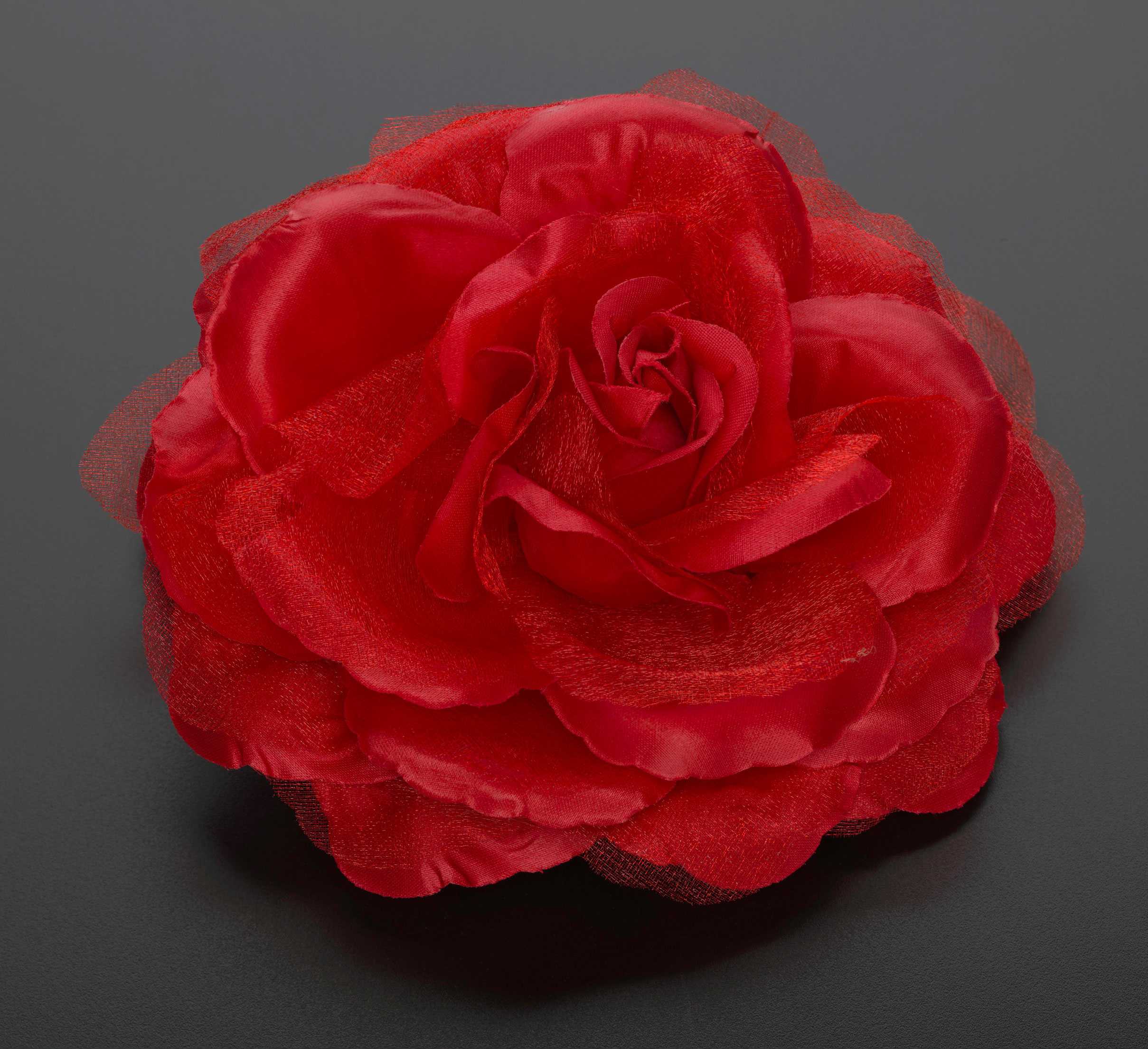 A bright red silk rose with many petals. The rose looks realistic.