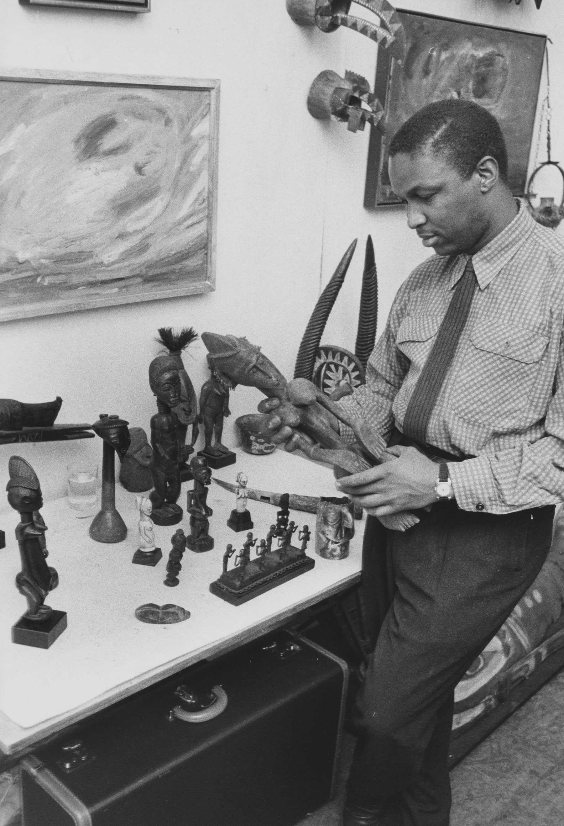 A person examining various sculptures and masks on a table in an art display.