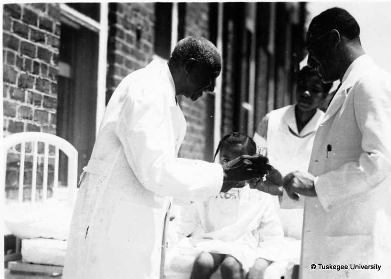 Black and white photograph of George Washington Carver administering a Penol to a young girl.  A female nurse and male doctor assist in the injection.