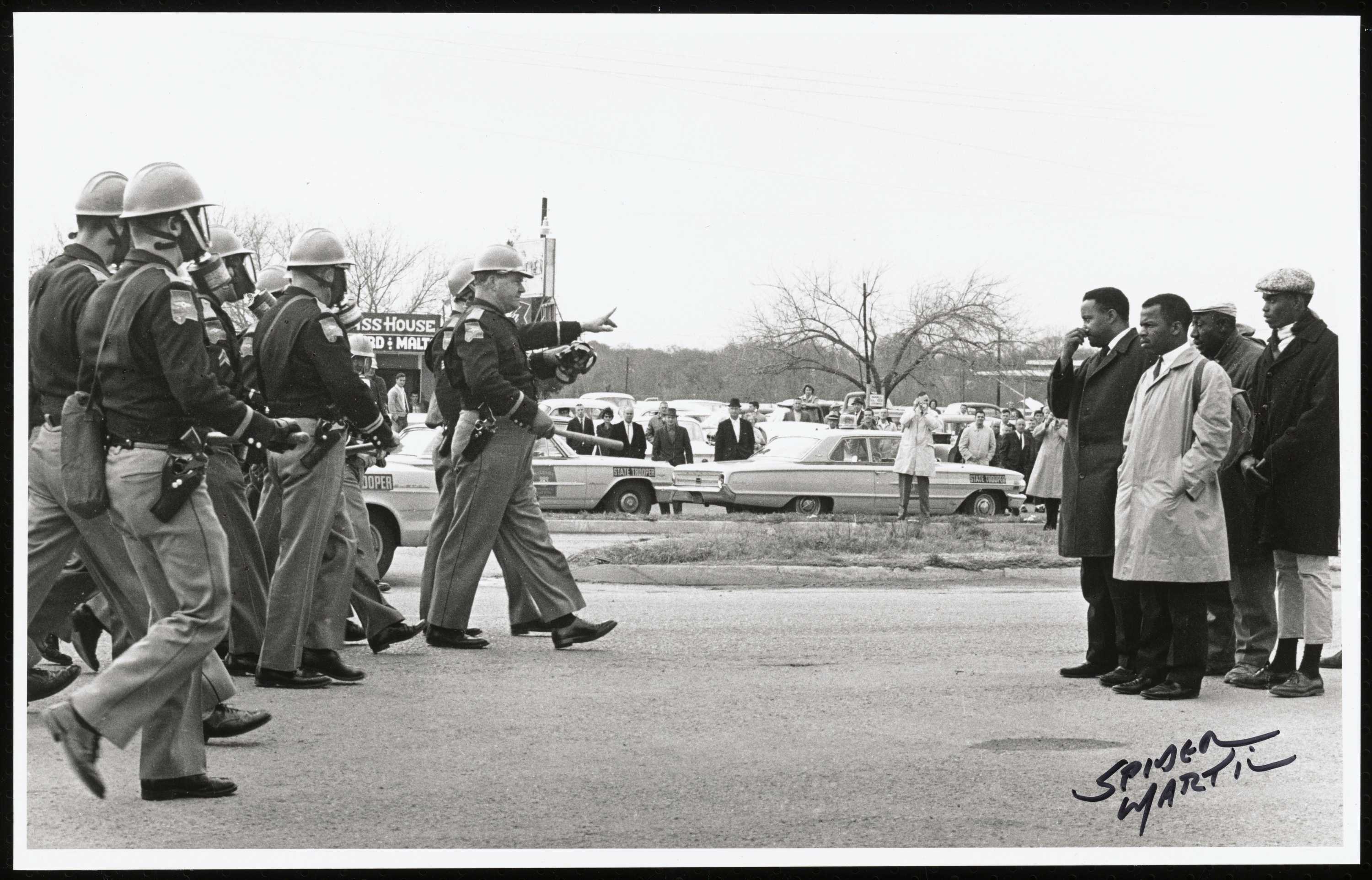 A black-and-white photograph of Alabama police officers approaching Civil Rights marchers. White onlookers can be seen in the background between the two groups. This photograph may be a prelude to 2011.14.5.