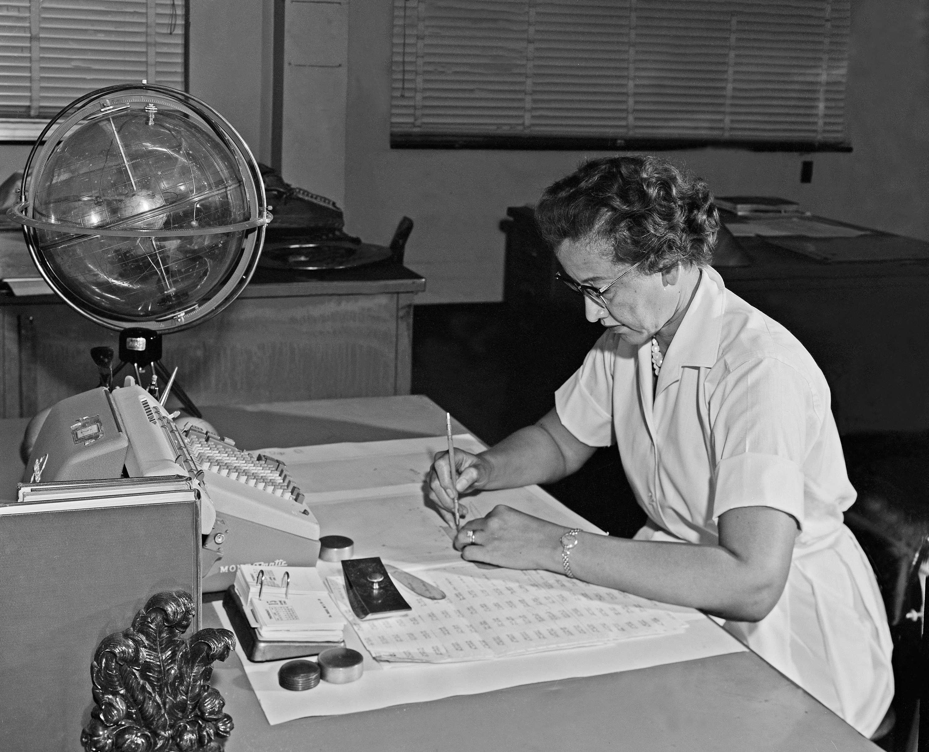 Katherine Johnson is focused on the papers in front of her as she works at a desk. She has a pencil in her hand.
