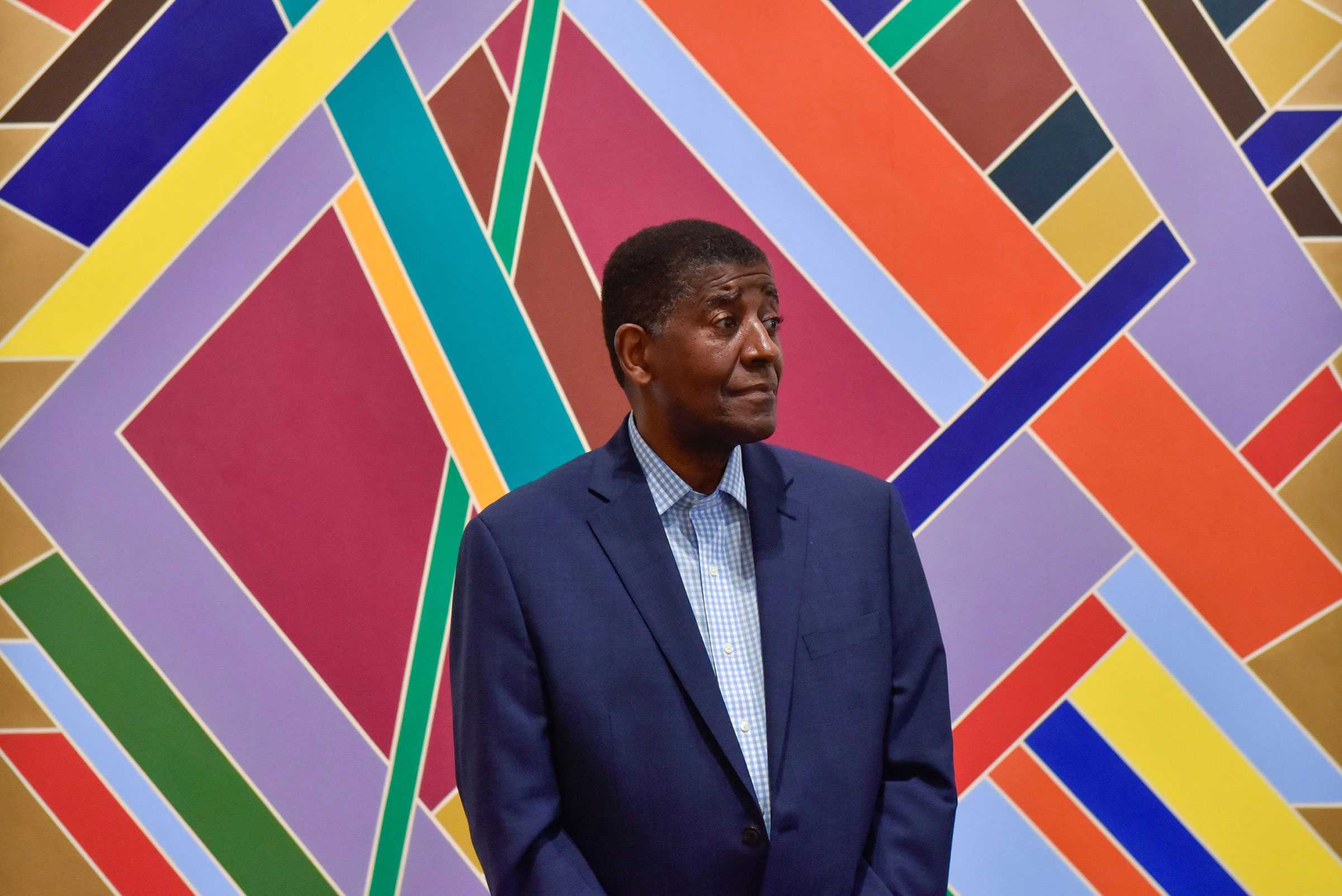 Man in a suit standing in front of a colorful geometric mural.