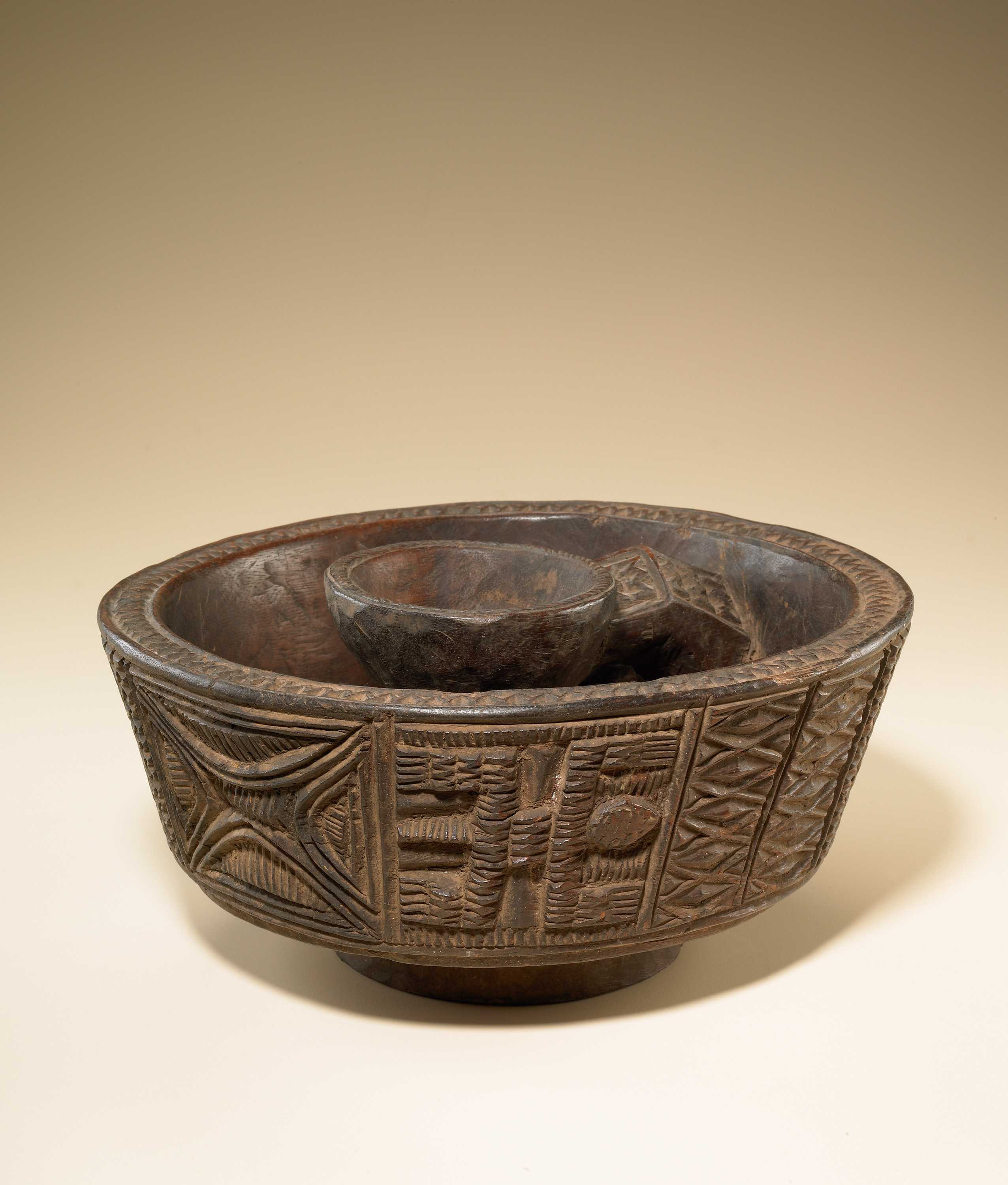 A dark wooden bowl carved with a geometric motifs and designs around the sides and edges of the bowl.