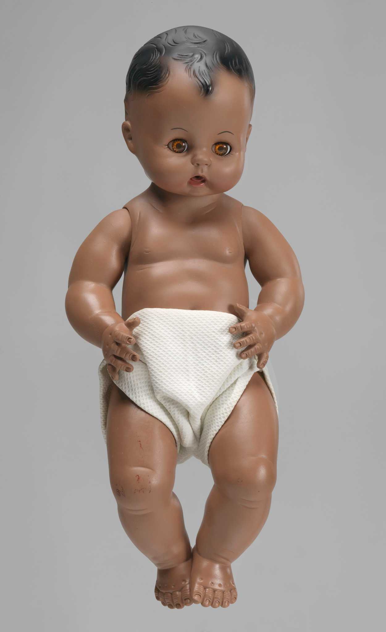 An African American baby doll. The doll has open- and close- eye functionality and wears a cloth diaper.