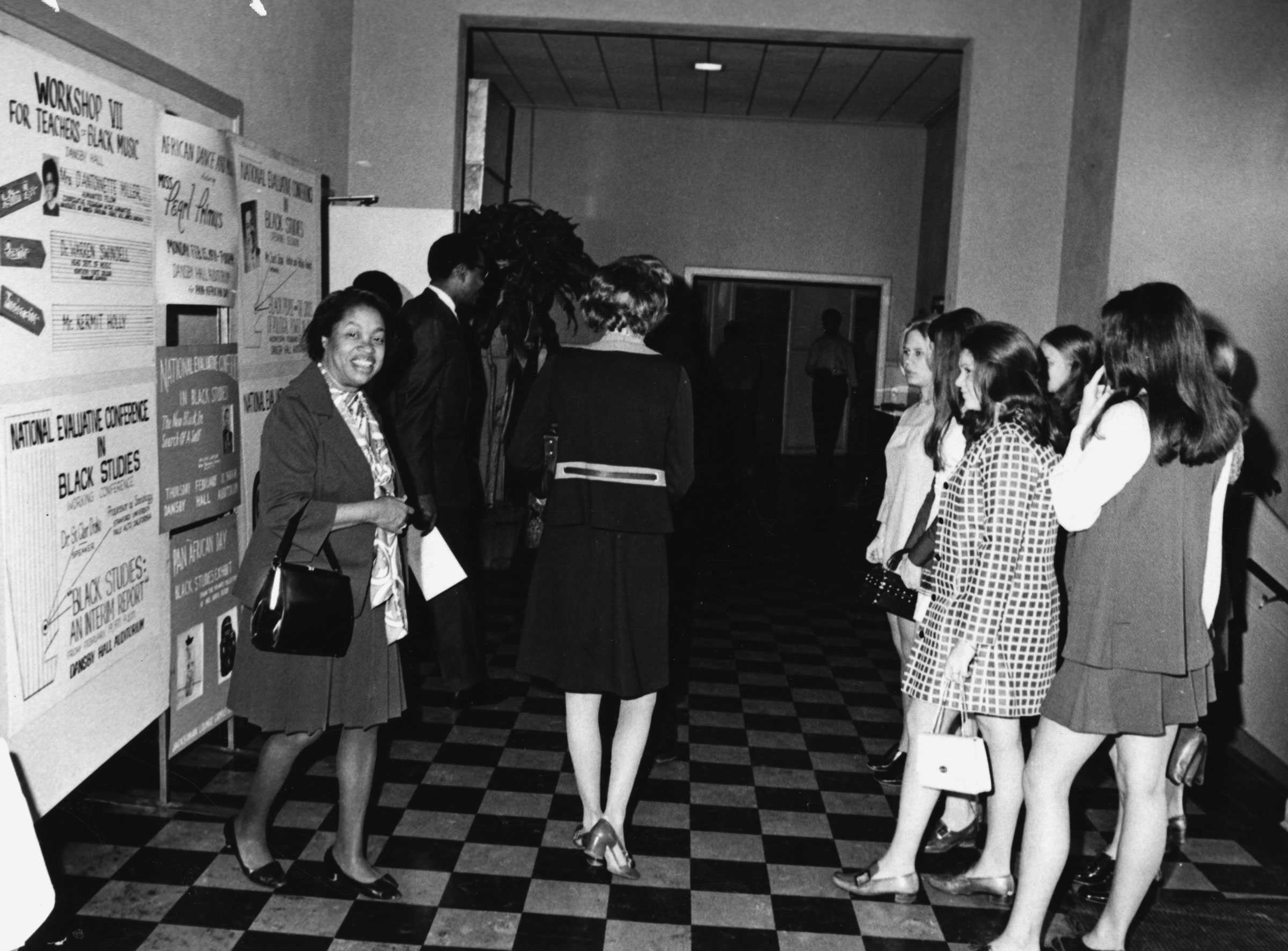 Photo of a group of people viewing posters on Black studies, with a woman smiling at the camera.
