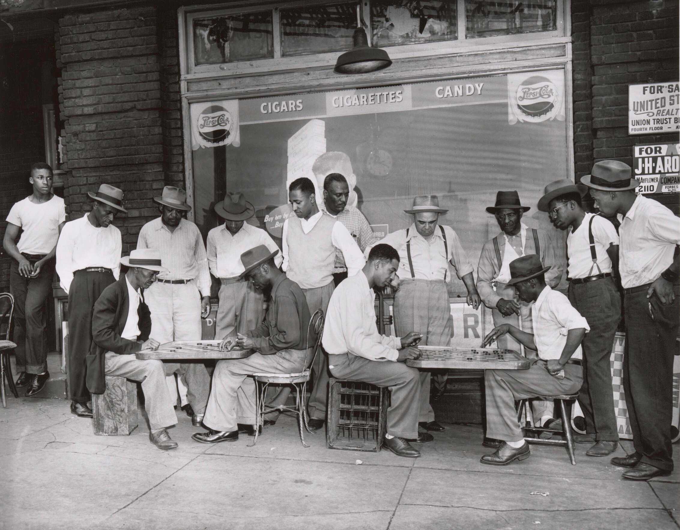 A black and white photograph of a large group of men observing two separate games of checkers.