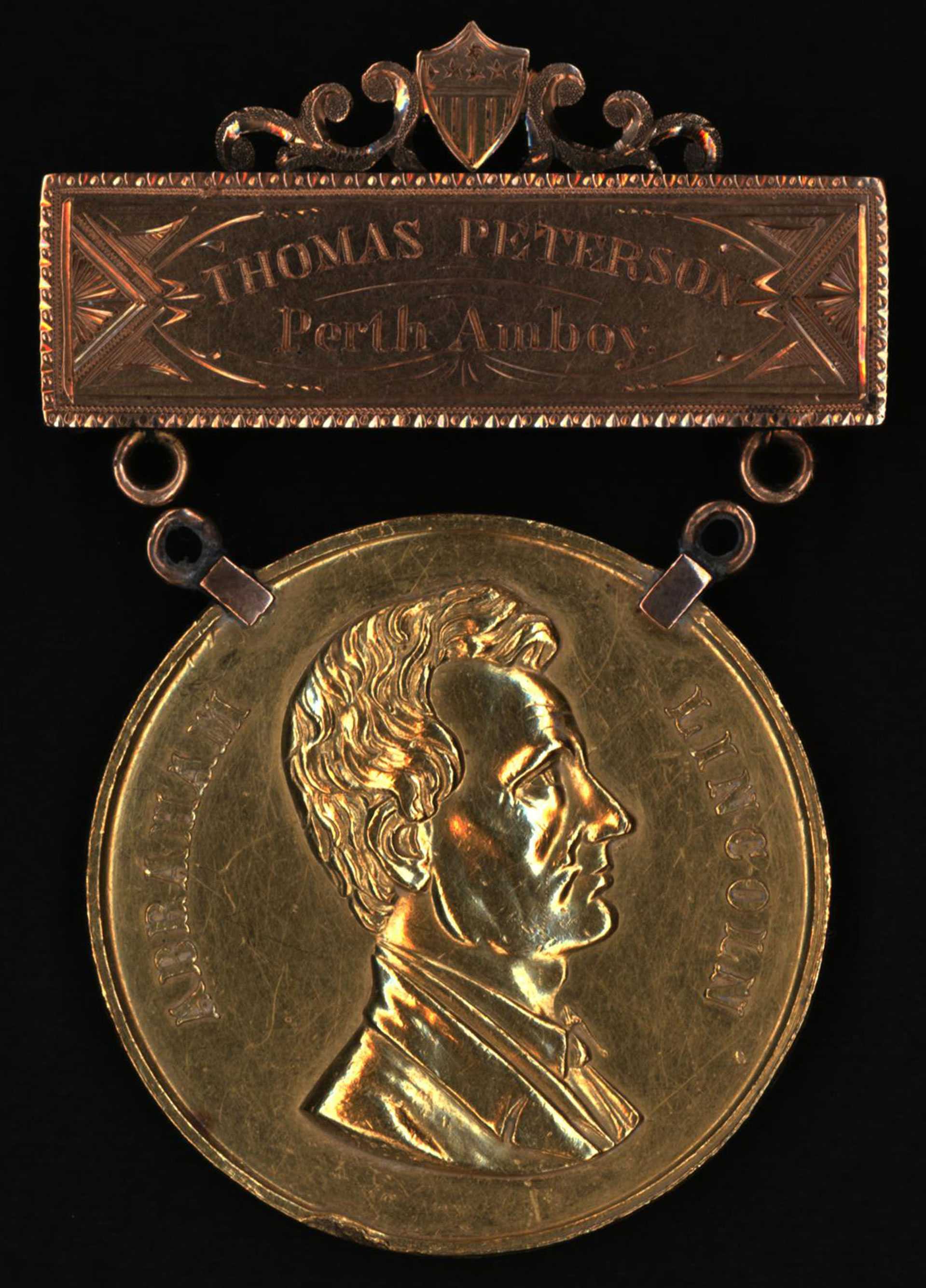 Gold medal embossed with the profile of Thomas Mundy Peterson.  The medal dangles from a gold bar engraved with " Thomas Peterson, Perth Amboy"