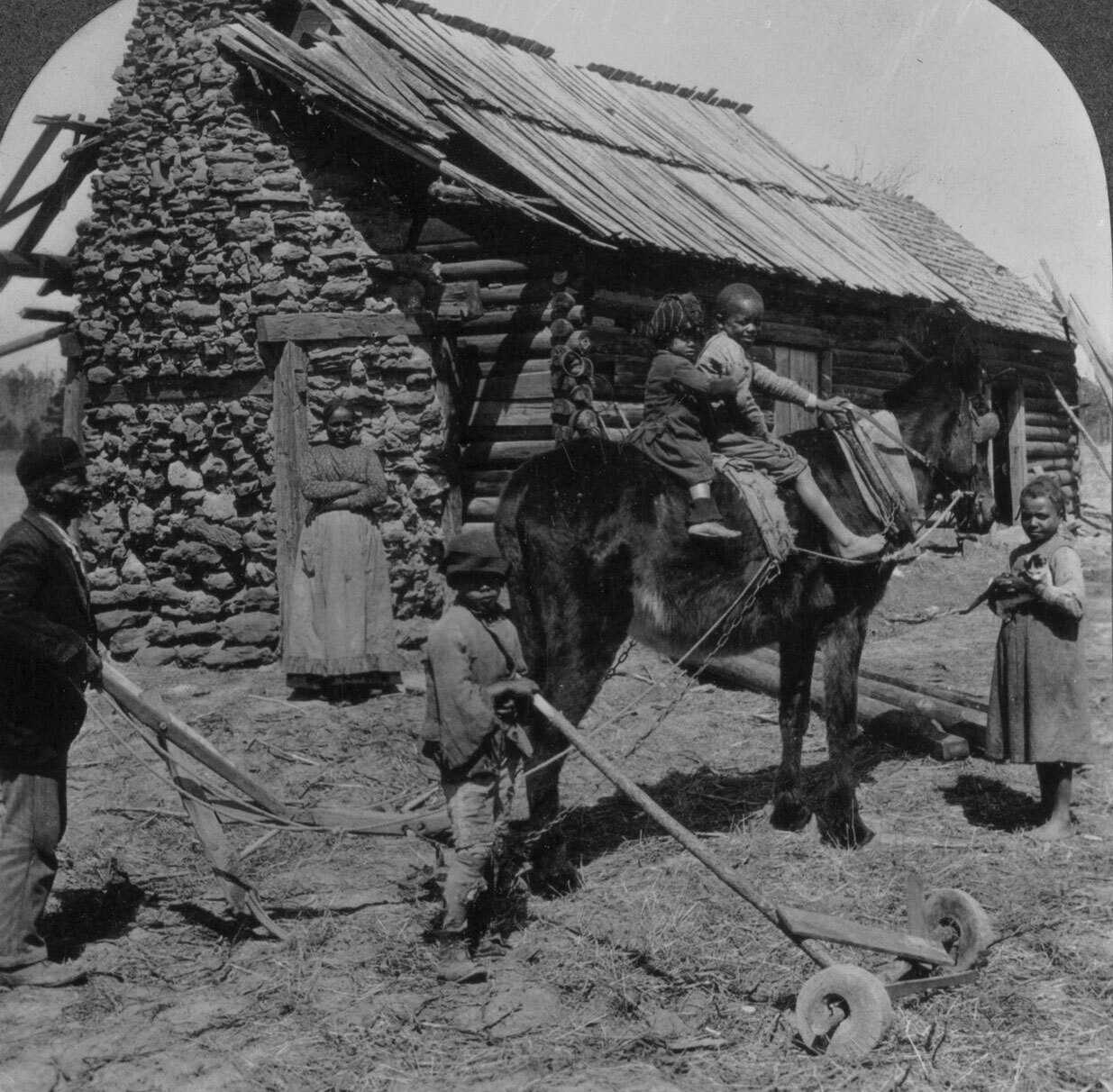Black and white stereograph of a family in front of a log house.