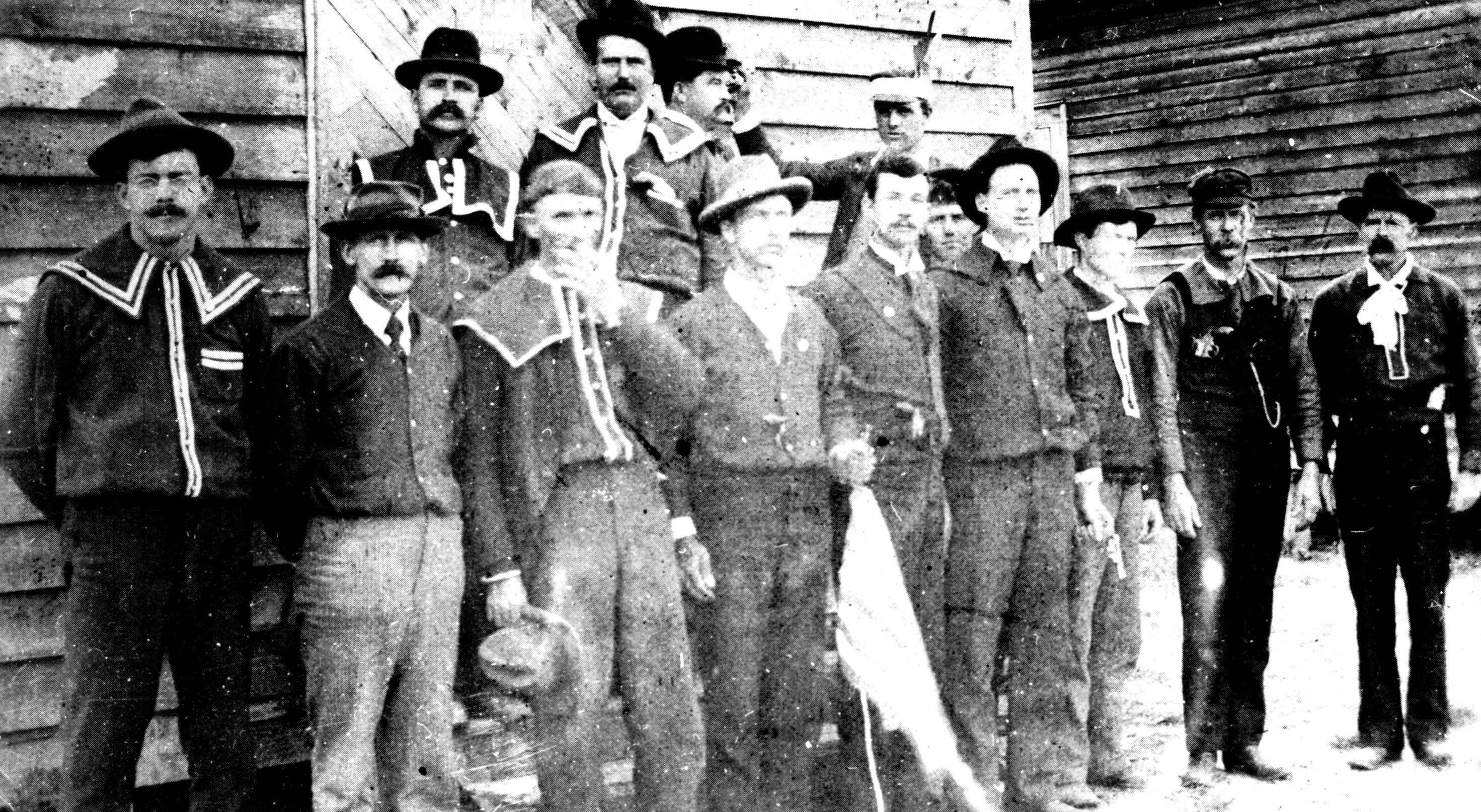 A slightly overexposed photograph of a group of white men dressed similarly stand outside polls.