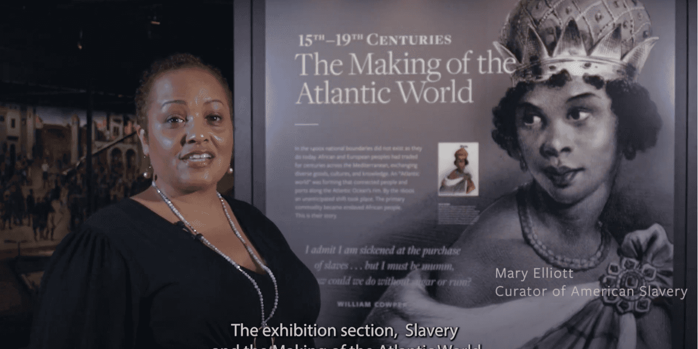 The curators stands in front of a Slavery and the Making of the Atlantic Word sign within the museum.