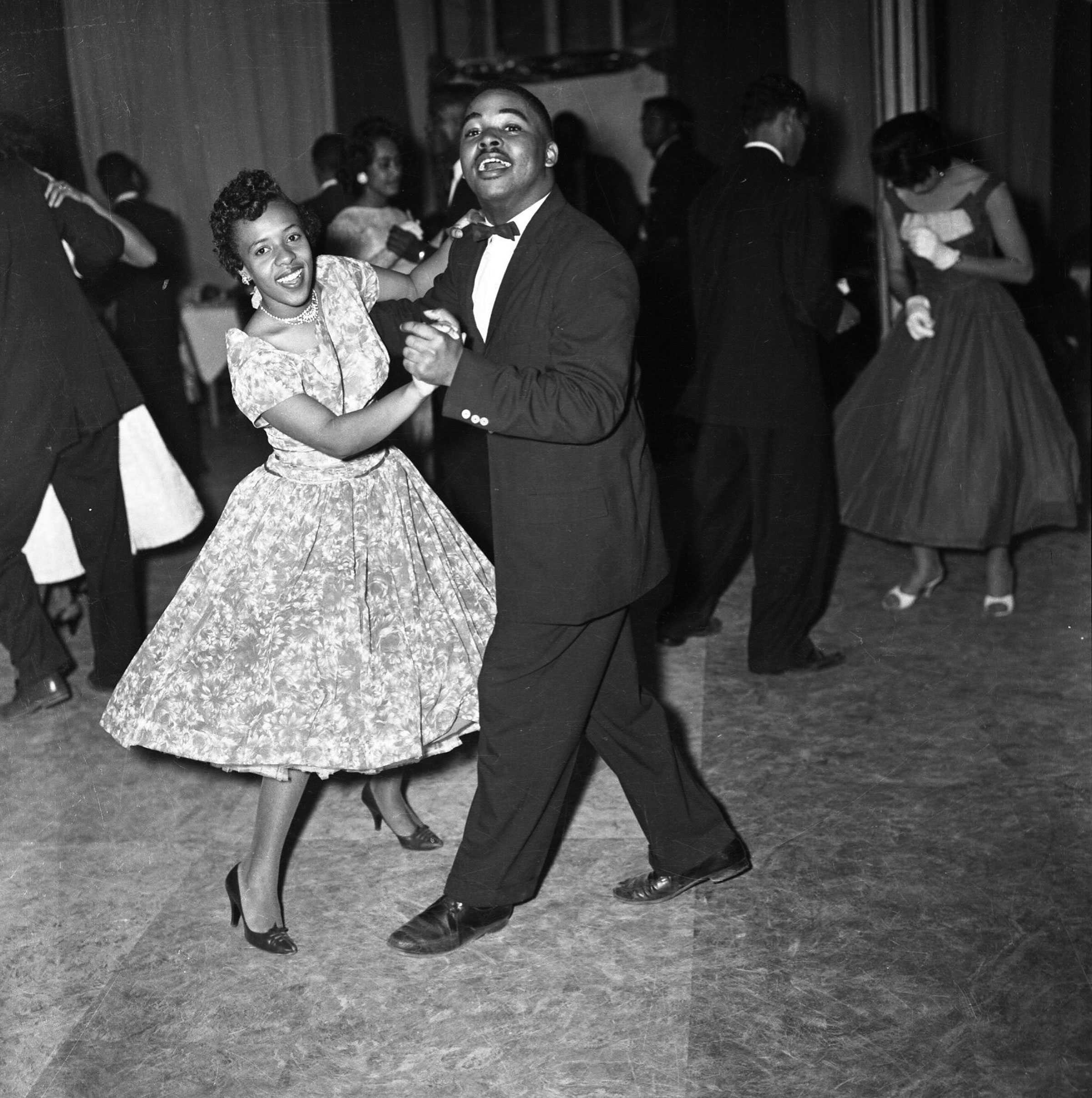 Black-and-white photo of a couple dancing at a formal event, surrounded by other dancing couples.