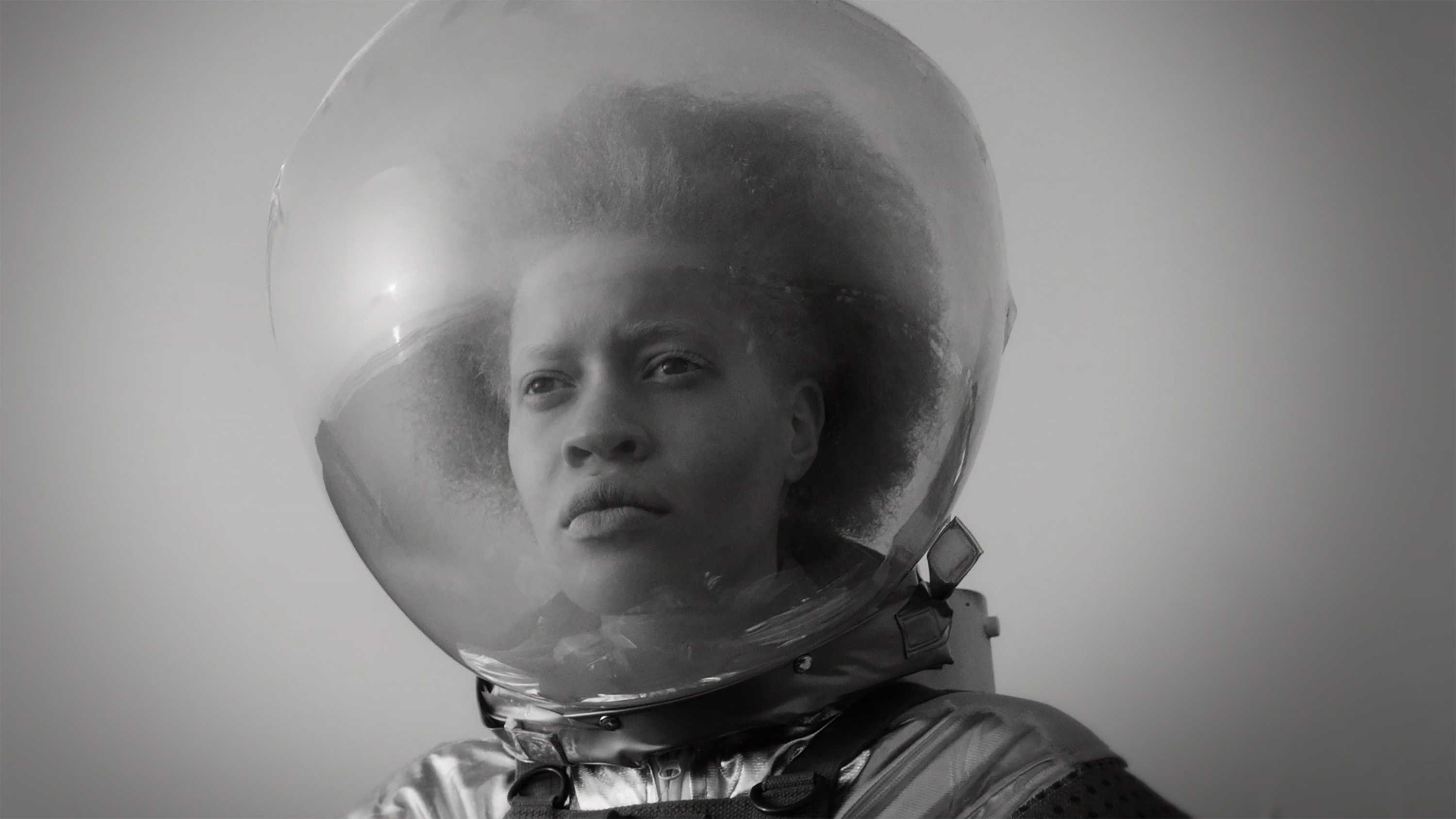 Black and white still image of a black woman in a space suit and helmet.