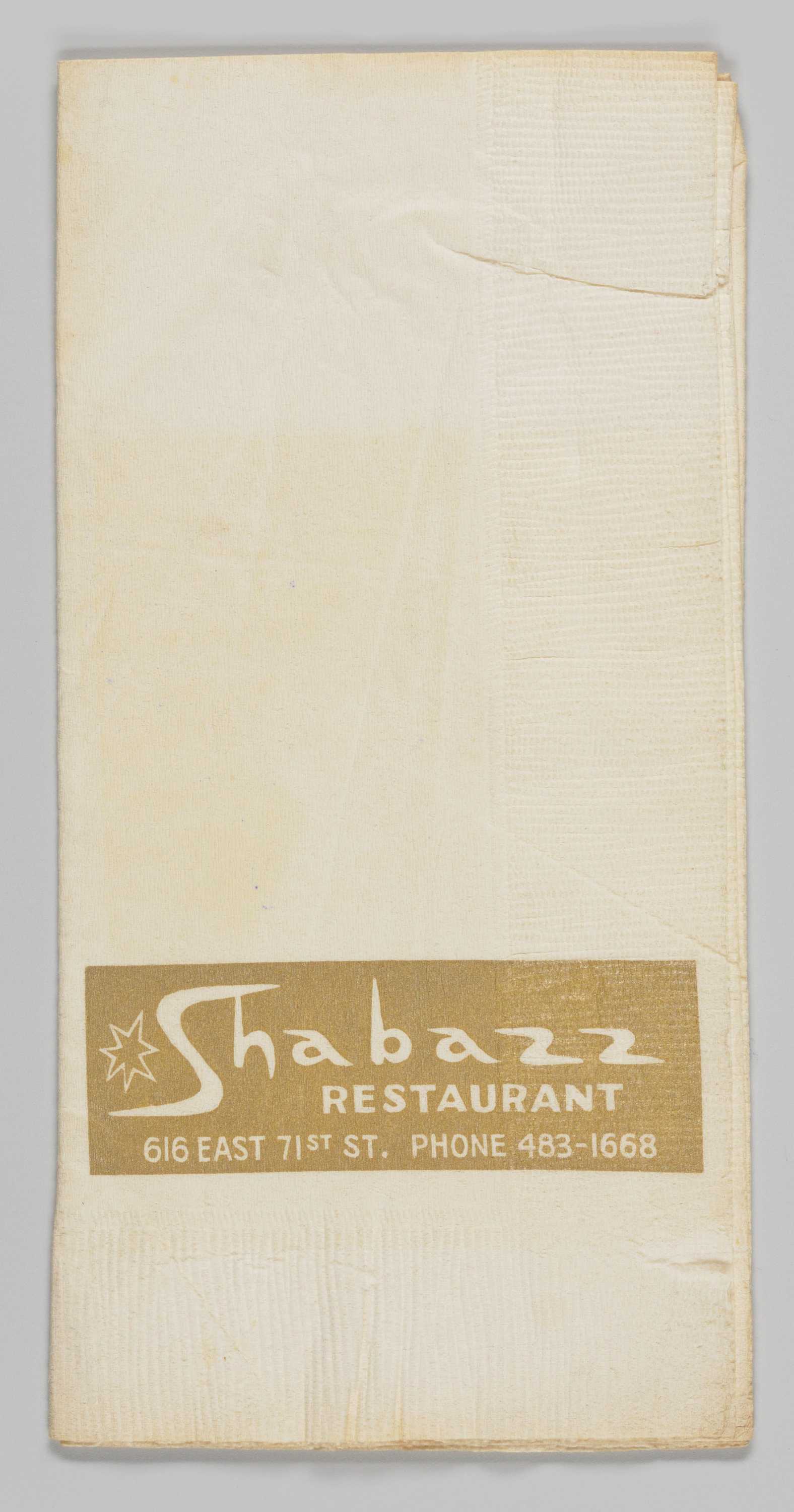 This rectangular Shabazz Restaurant paper napkin is off white with a light brown horizontal rectangular field on the lower third portion of the front