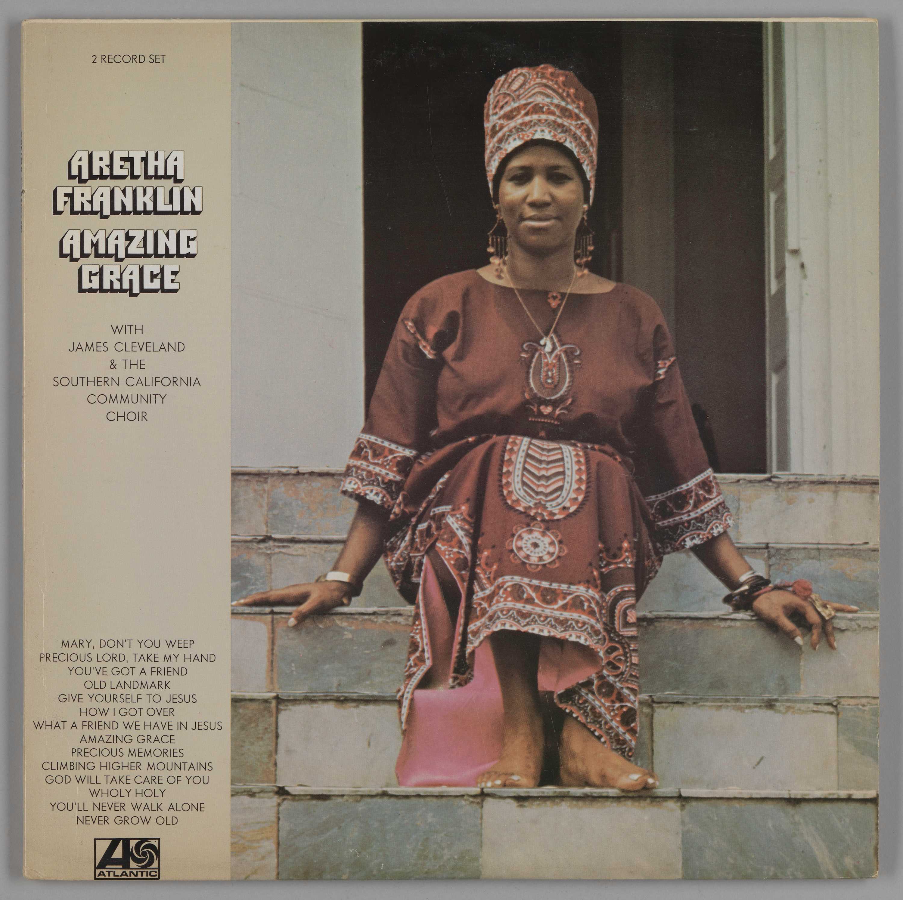 Image of the album jacket for Aretha Franklin's album Amazing Grace, featuring an image of Aretha Franklin sitting barefoot on steps in a pink dress and head wrap.