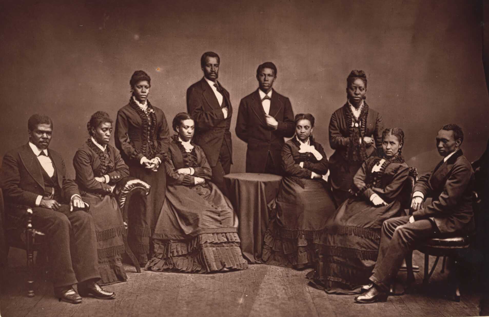 A black and white posed, portrait of Fisk Jubilee Singers. Some are standing while others are sitting.