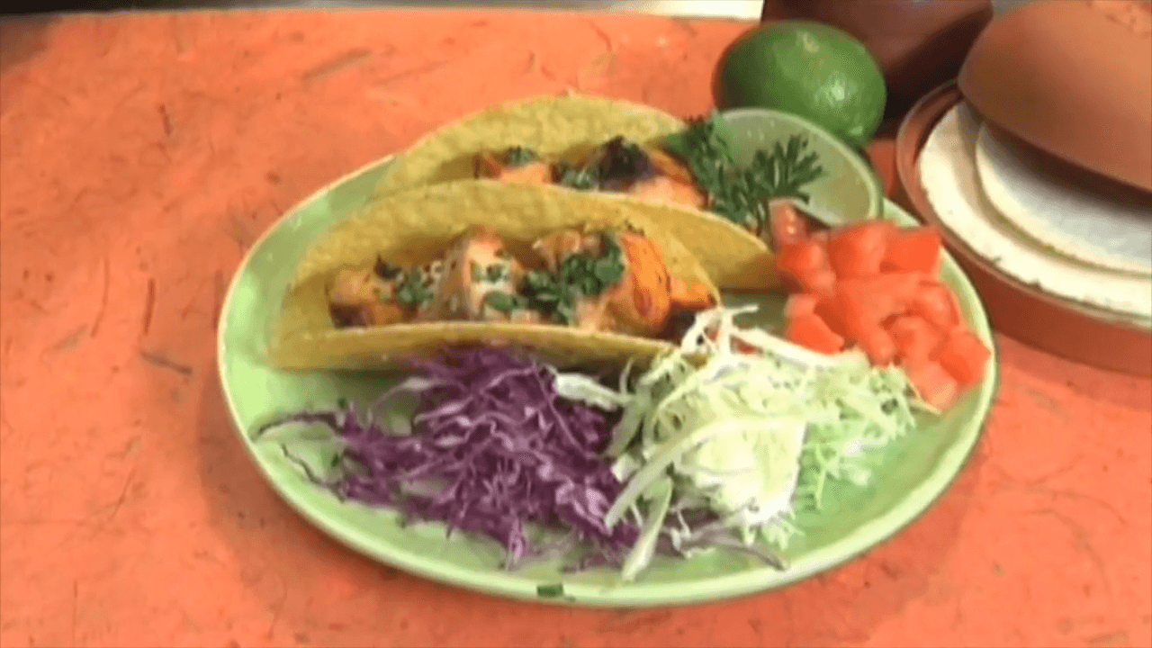 Two salmon tacos with cabbage and tomatoes on the are plated on a green plate.