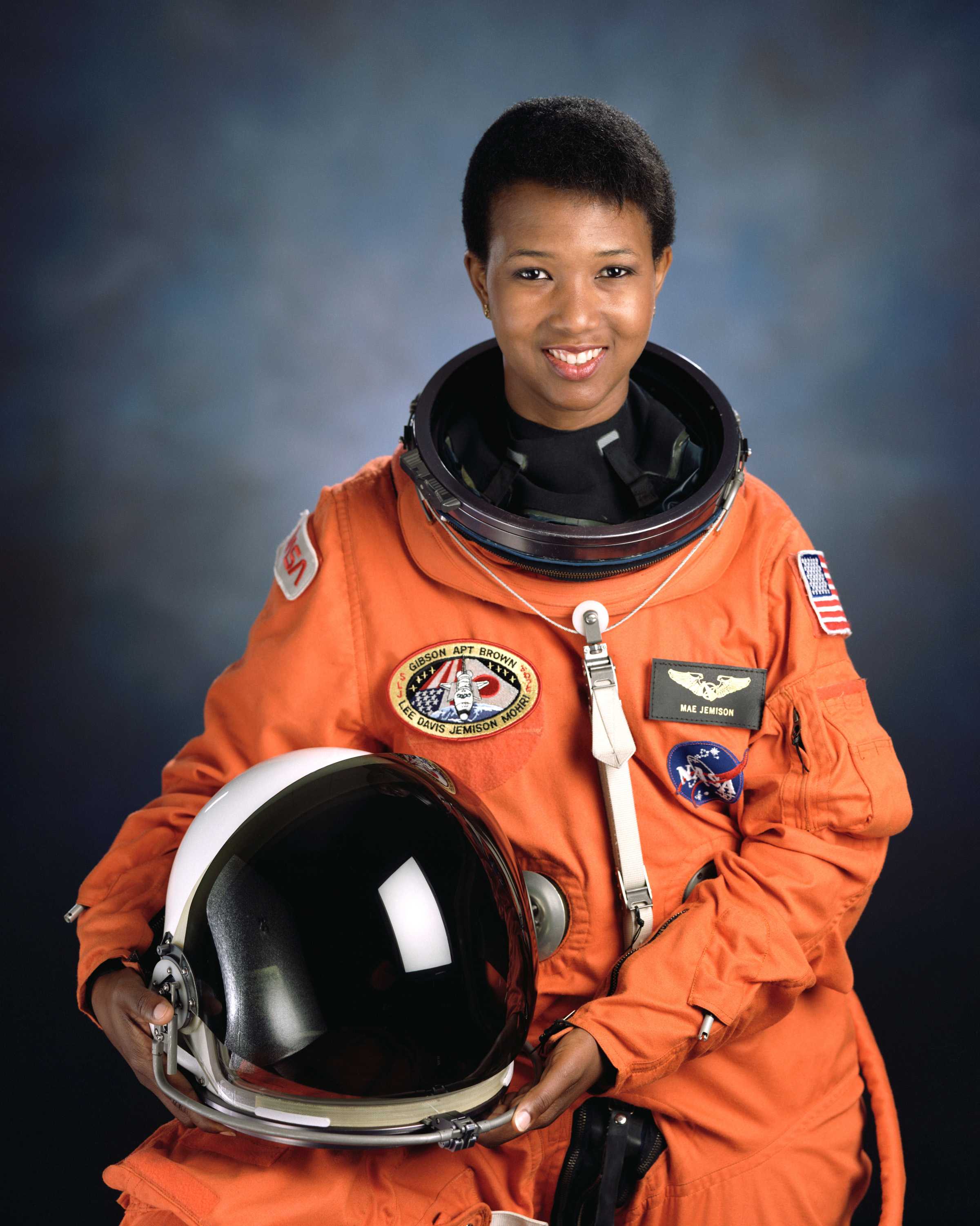 Jeminson is wearing a NASA orange space suit and holding a helmet as she poses for her portrait.