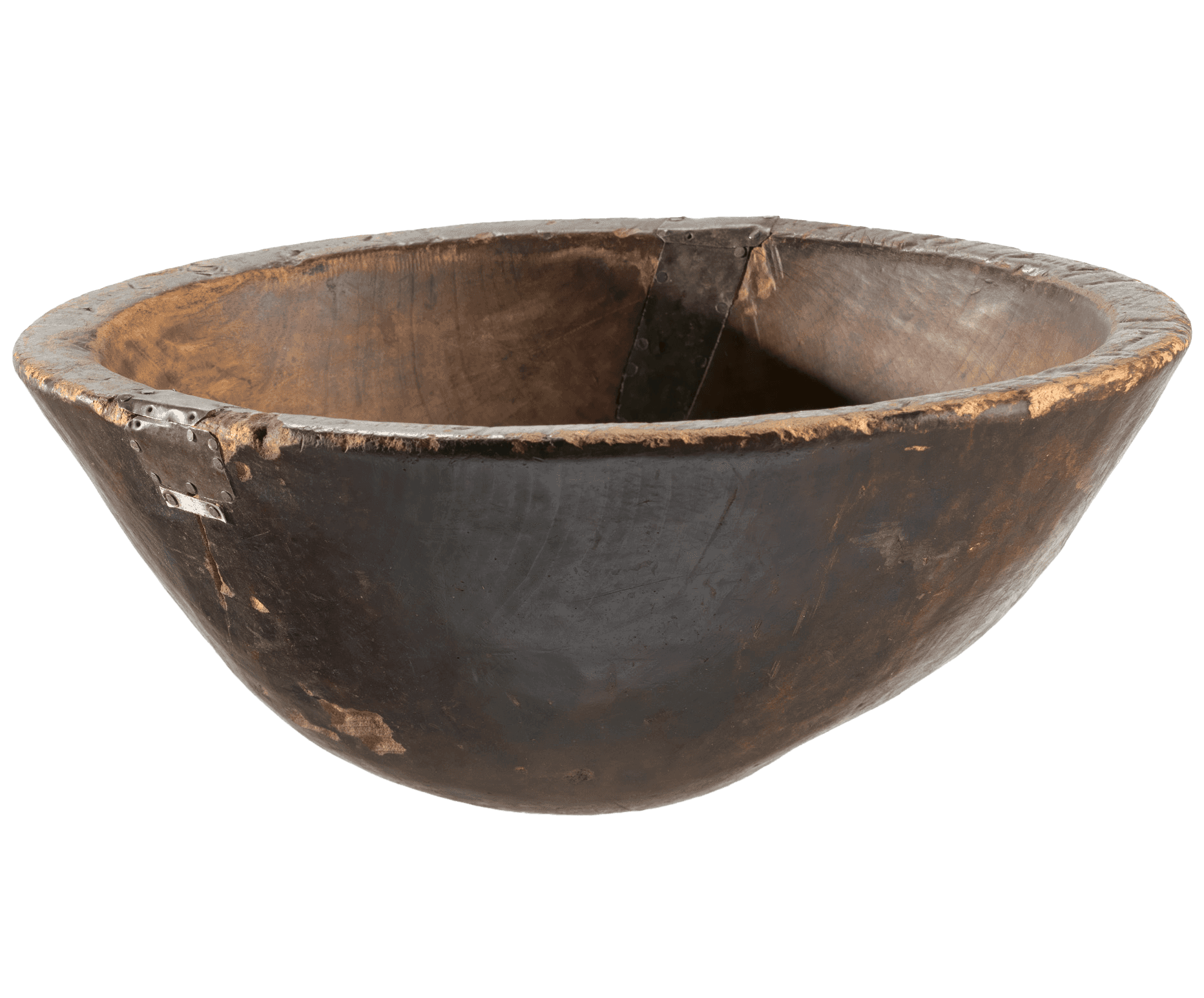 A large wooden bowl with an uneven shape and a rounded bottom. The lip is decorated with incised Adinkra symbols. Formed metal pieces were nailed over 2 separate cracks, acting as "patches." There is surface wear throughout, particularly on the bottom and around the lip.
