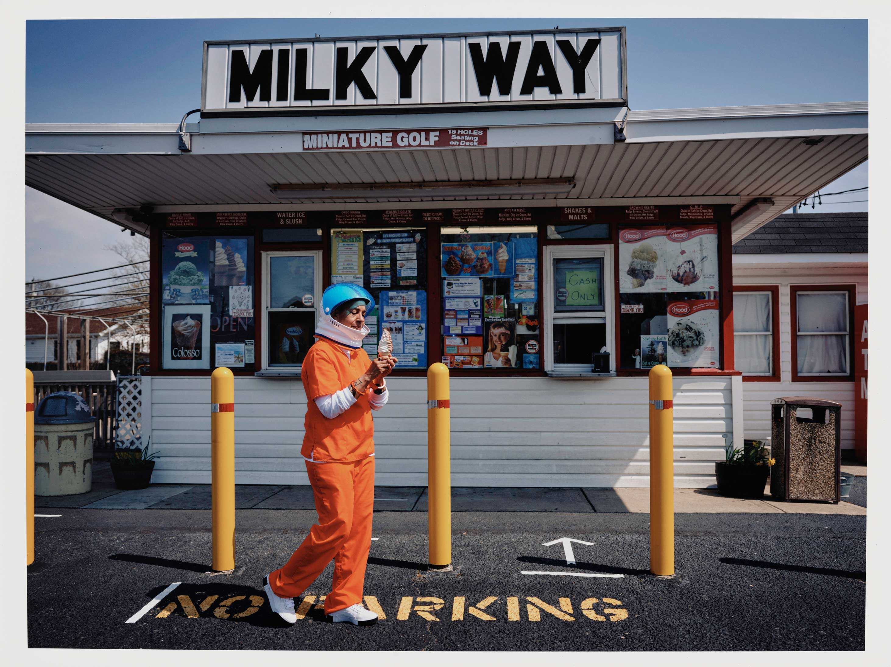 An escaped astronuat prisioner eating soft served ice cream from a small ice cream stand called the Milky Way.