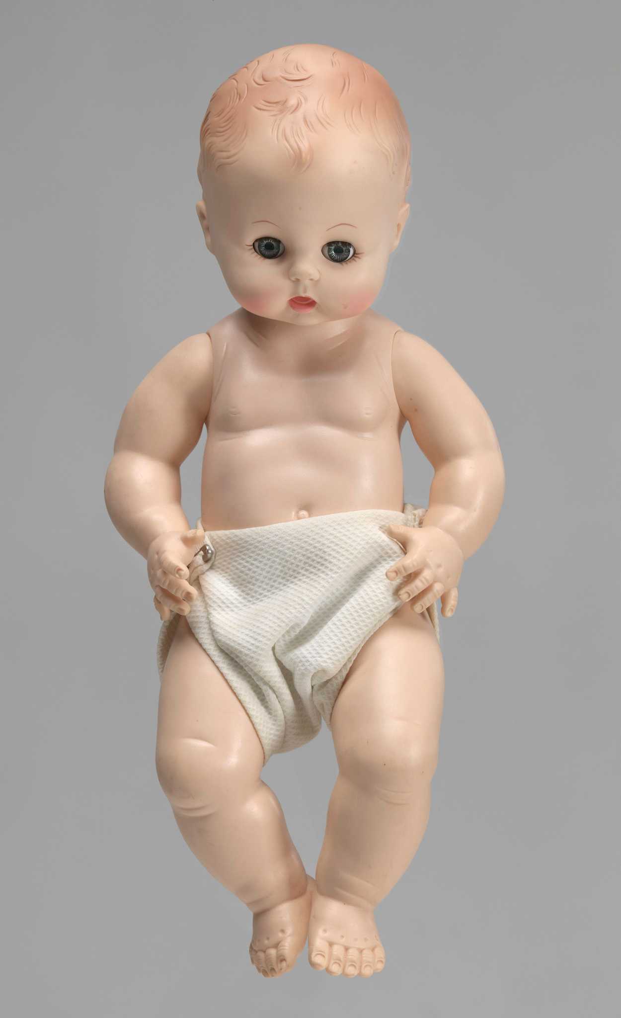 A white baby doll. The doll has open- and close- eye functionality and wears a cloth diaper.