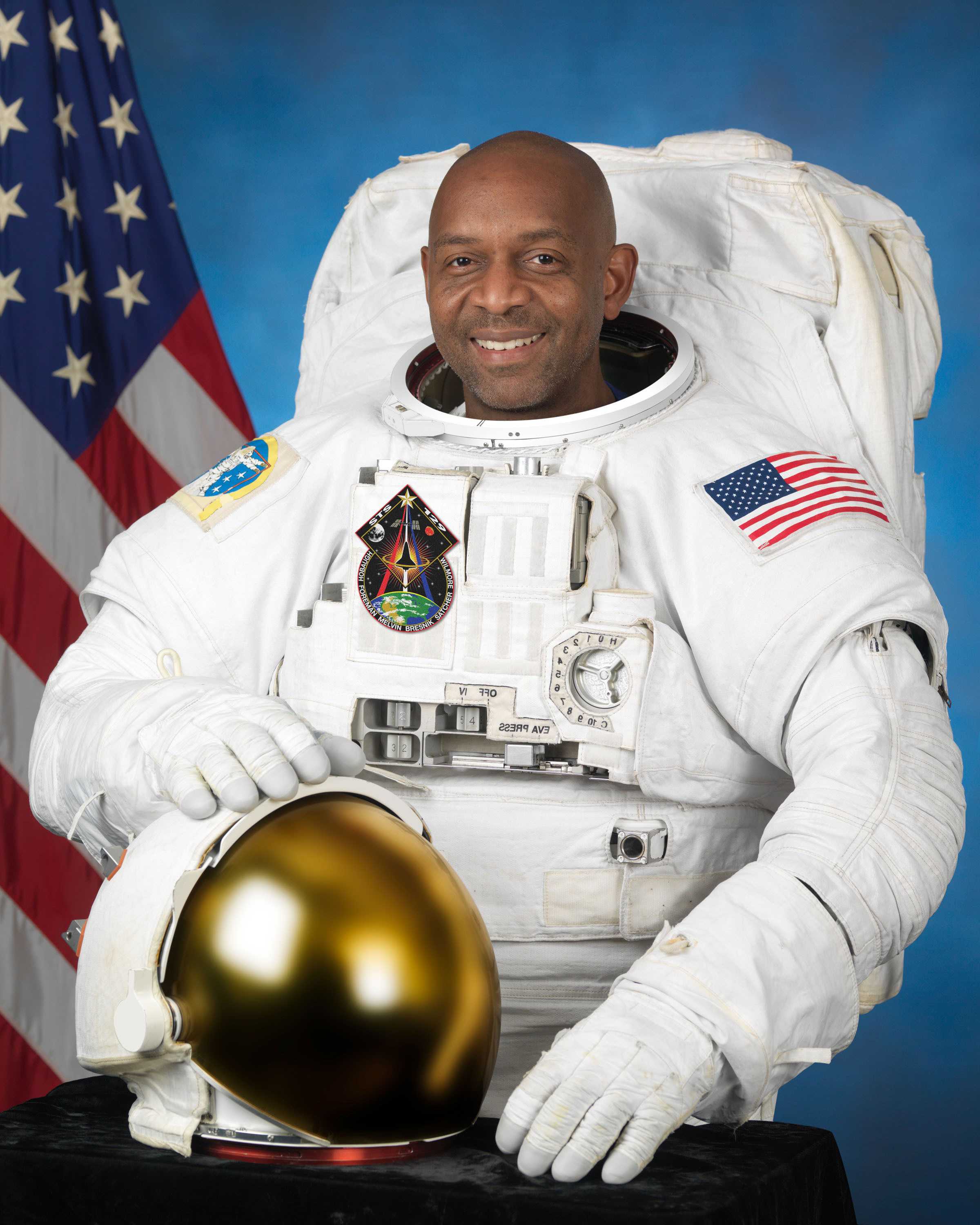 Robert Satcher poses for his portrait in a white NASA space suit while holding a helmet.