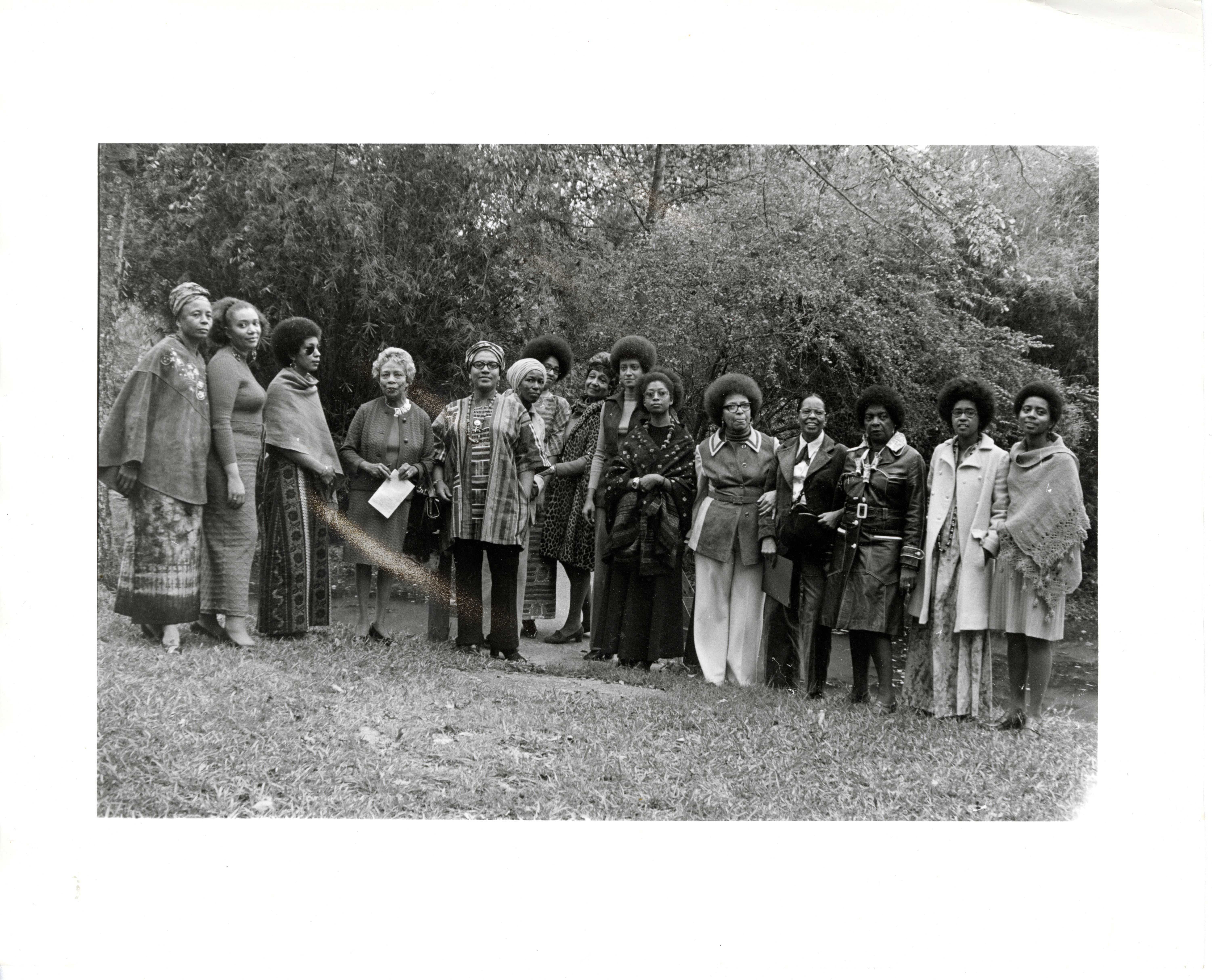 Black and white group portrait of about 15 unidentified women standing in a half-circle in front of a wooded area.