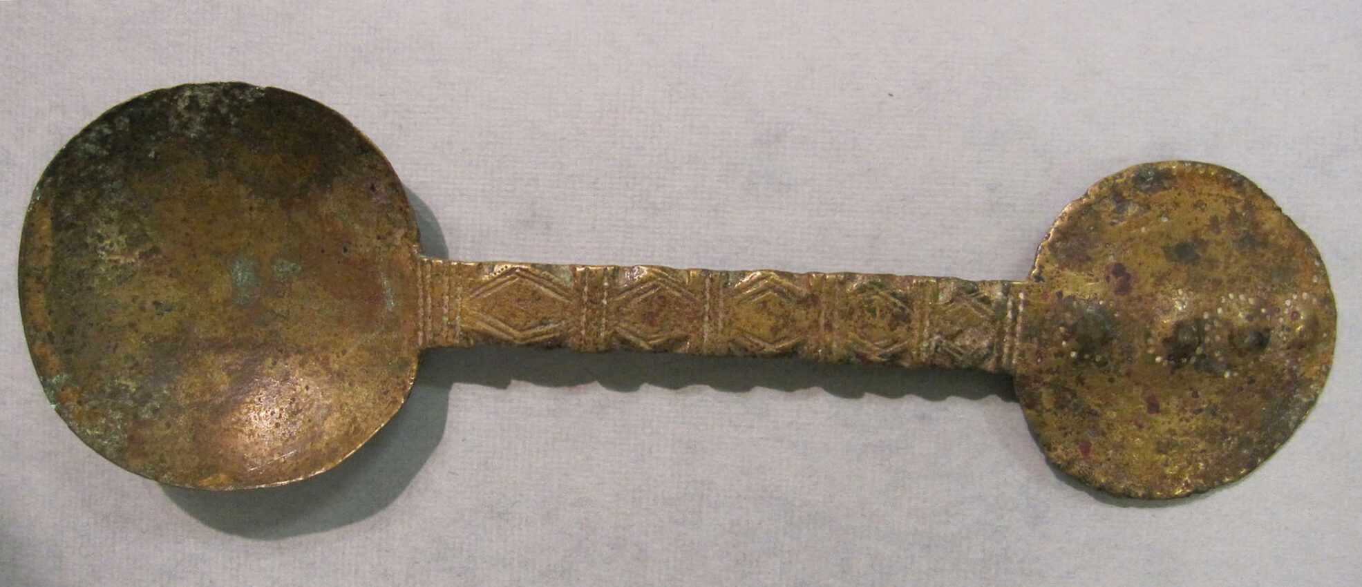 The Akan gold powder scoop on display against a light grey background. The scoop is a little tarnished.