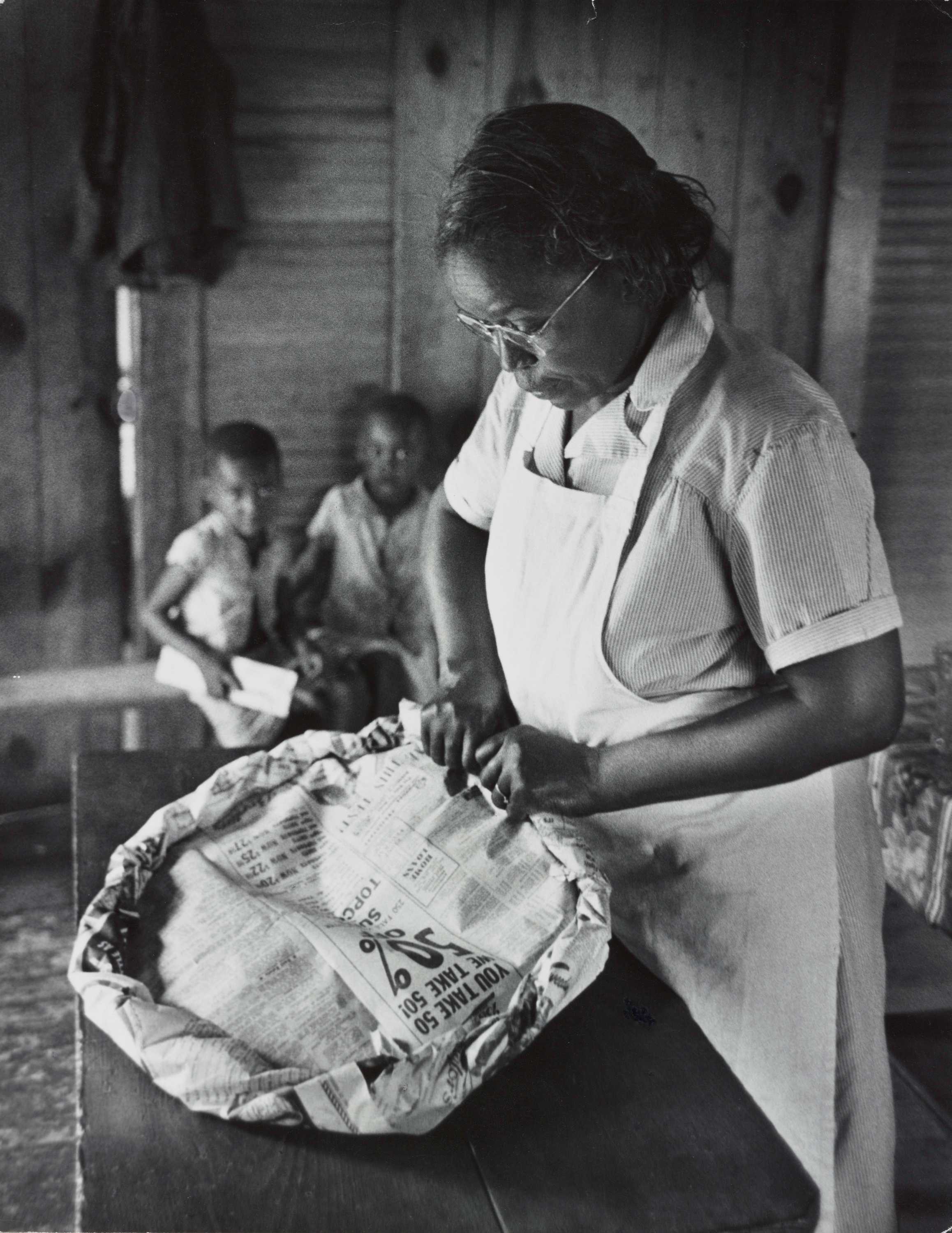 A black-and-white photograph of Maude Callen rolling a newspaper into a delivery pad.