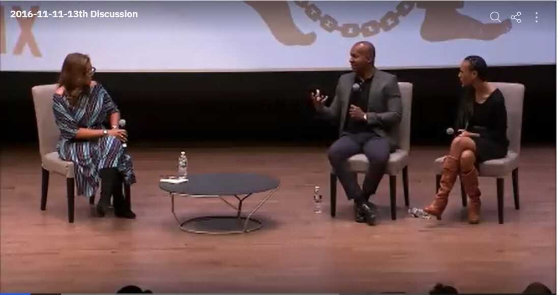 Screenshot of film showing 3 person panel seated on a stage.