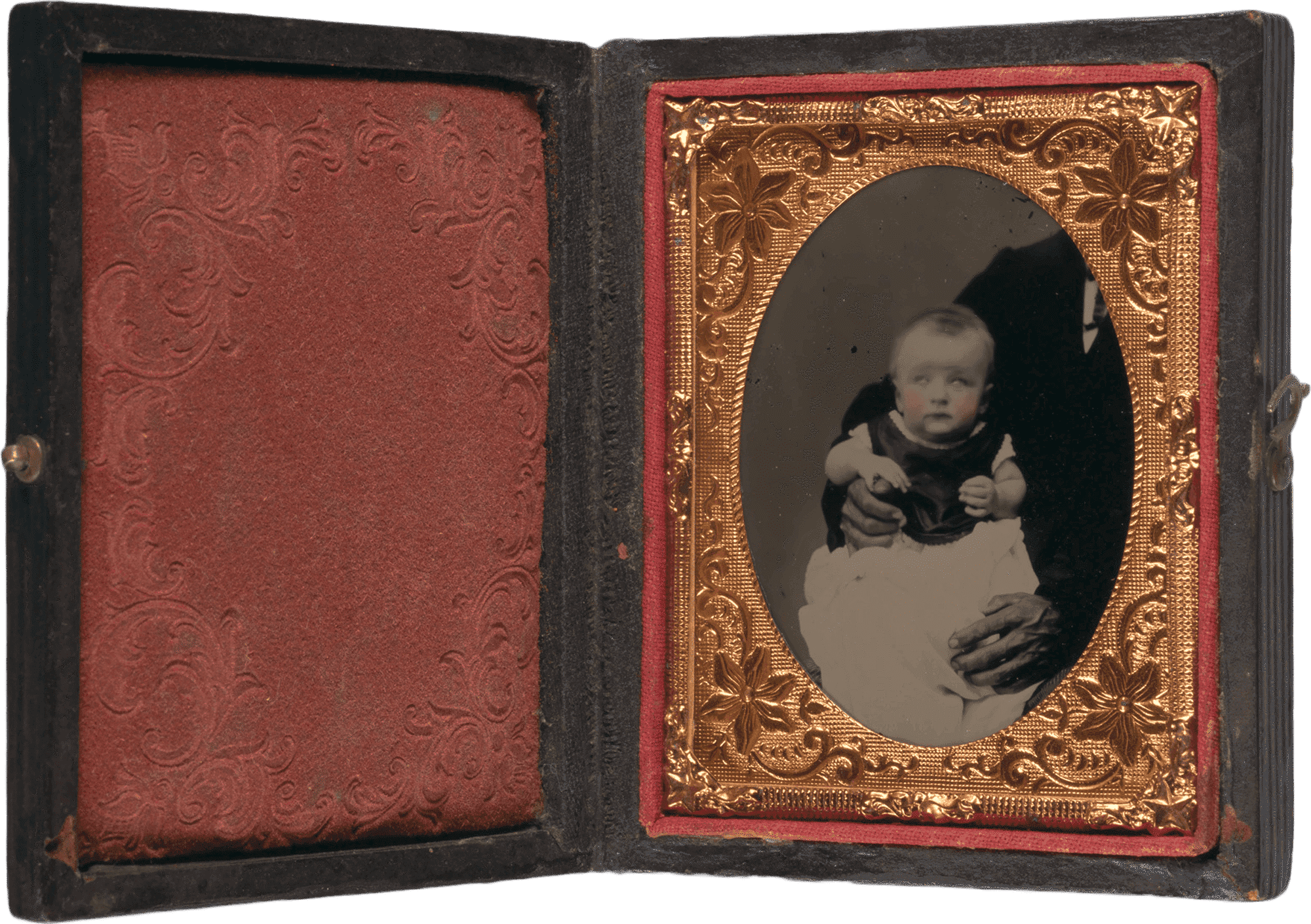 This 1/9 plate cased ambrotype depicts a white baby being held for the camera by a black man whose shoulder and hands are visible, but is otherwise unseen. The baby's cheeks have been tinted pink. The photograph is in a decorative copper-colored metal oval frame with a floral, star, and scroll motif and is held in a brown case with red textile lining. There are decorative impressions on the front and back of the case, which fastens with a small metal hook and eye closure along one edge.