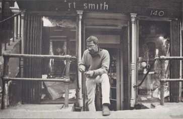 Black-and-white photo of a person standing on steps in front of a storefront.
