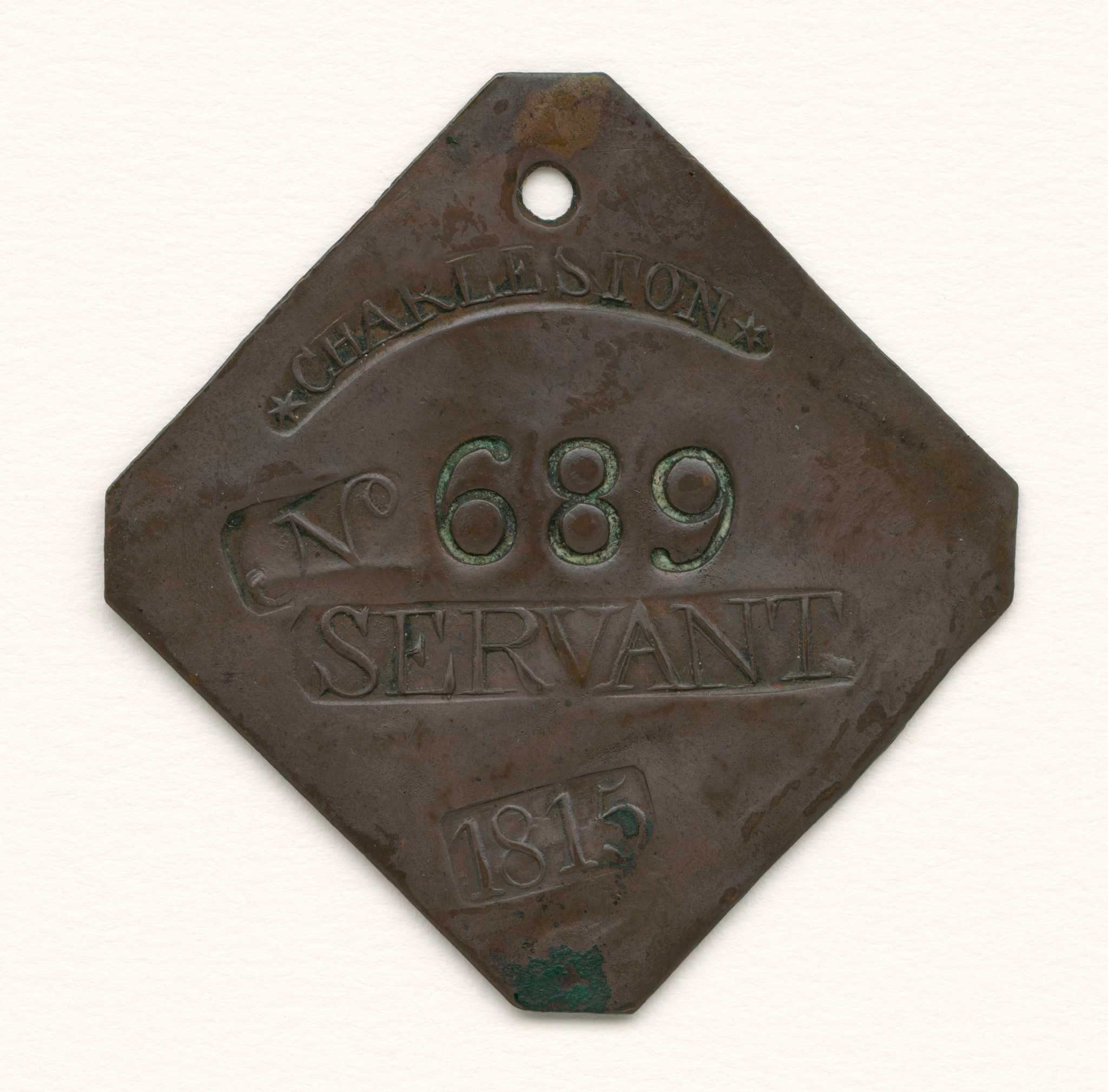 A flat diamond-shaped tag with clipped corners and a hole at the top for suspension. “LAFAR” hallmark punched on the back. The elements on the front are as follows (top to bottom): "*CHARLESTON*" in a lunate bar punch; "No" in a square punch followed by an incuse "689" in deep individual punches; "SERVANT" in a rectangular punch; and "1815" bar punched at somewhat of an angle. The condition on this tag is extremely fine with well-defined elements, smooth surfaces, and an even medium brown patina. There is just a bit of verdigris at the bottom.