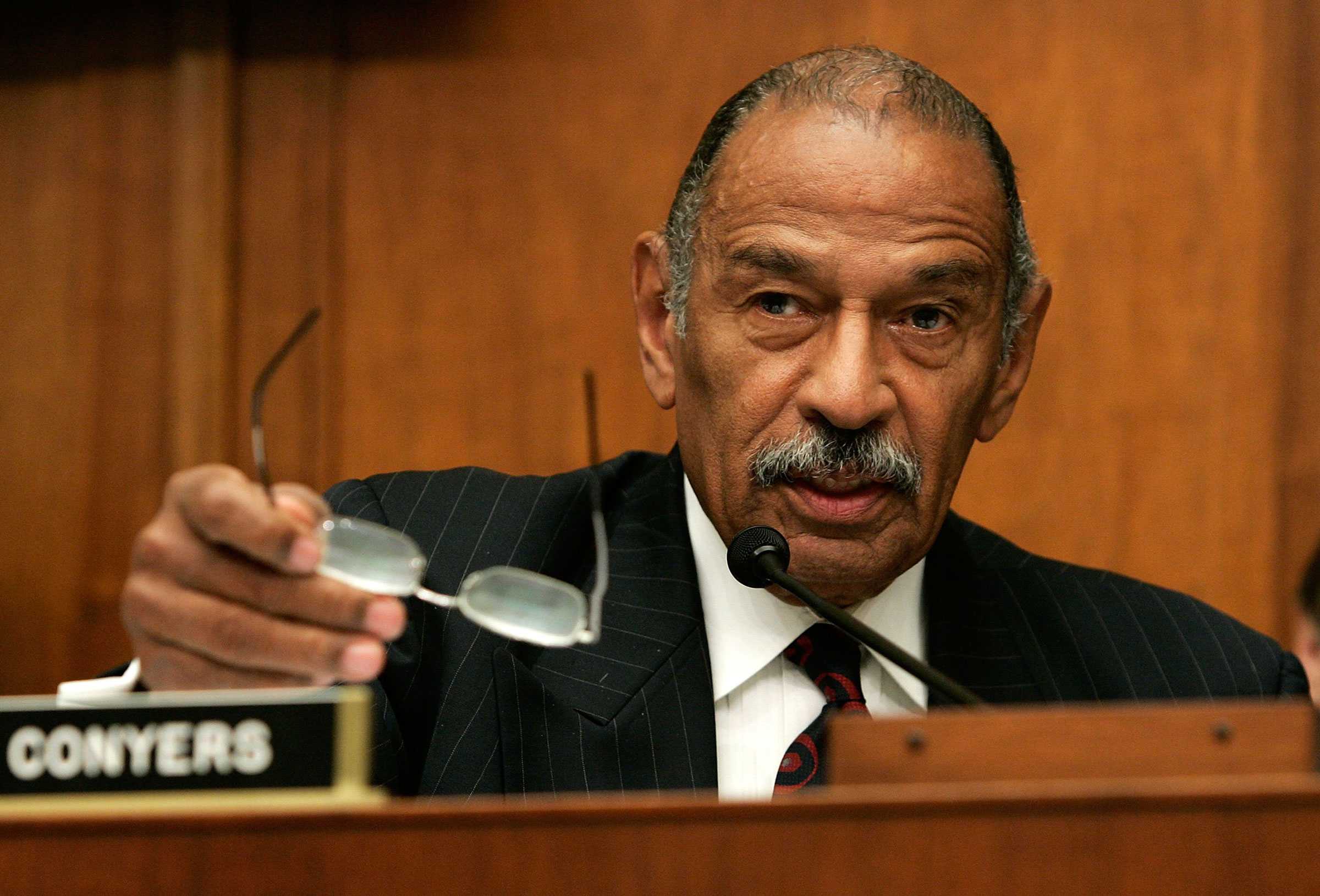A close up photo of John Conyers talking. He is speaking have and have taken off his glasses.