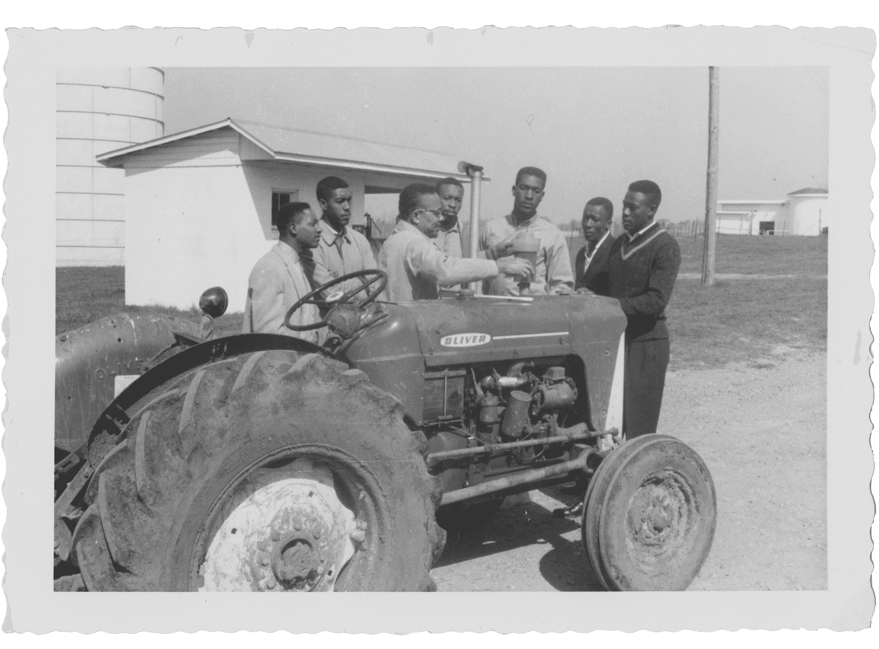 A group of men gathered around a tractor, with one man gesturing as if explaining something.