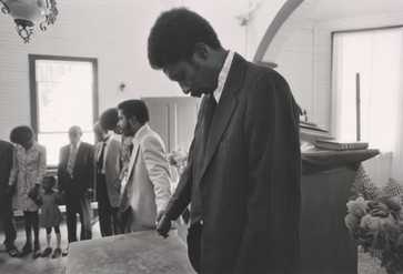 This gelatin silver print depicts a black and white image of church members praying.