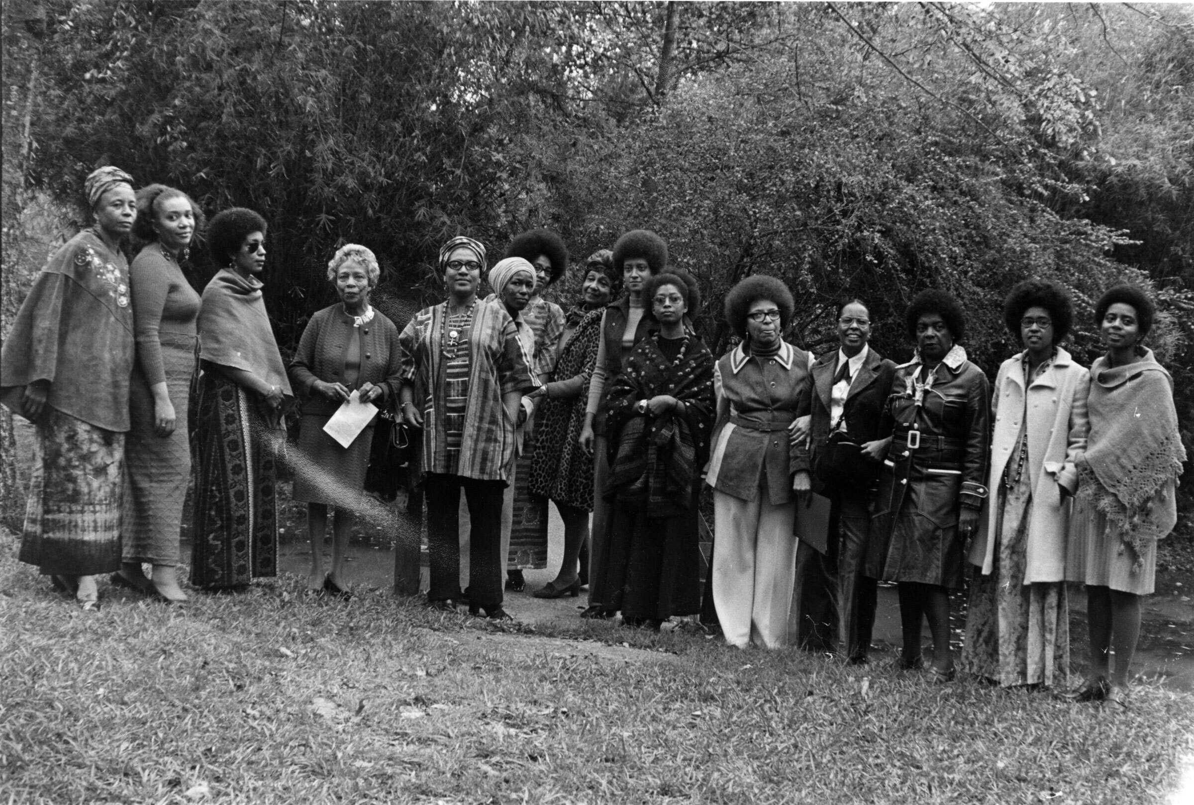 Black and white group portrait of about 15 unidentified women standing in a half-circle in front of a wooded area.