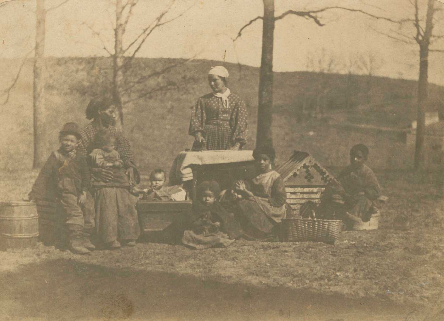 An albumen print on paper with a purple, reddish-brown hue depicting two adult women and seven children pictured, from left to right: William, Lucinda, Fannie (seated on Lucinda's lap), Mary (in cradle), Frances (standing), Martha, Julia (behind Martha), Harriet, and Charles or Marshall. Lucinda Hughes and Frances Hughes were sisters-in-law through Frances's husband David. The group is posed outside in front of bare trees, one woman is posed as if ironing. Baskets and a dog or doll house are placed around the group. The women and their children were enslaved at the time this photograph was taken on a plantation just west of Alexandria, Virginia, that belonged to Felix Richards. Frances and her children were enslaved by Felix, while Lucinda and her children were enslaved by his wife, Amelia Macrae Richards.

On the recto, an inscription is written in pencil on the paper mount below the image that reads: "Felix Richards slaves". On the verso, an inscription is written in pencil along the top center of the paper mount that reads "Felix Richards lived at 'Volusia' / Near Alexandria, VA." To the right of this inscription is more text written in pencil with a heavier hand that reads "101400 / 01-P-284". There is a pre-printed metallic oval on the verso.
