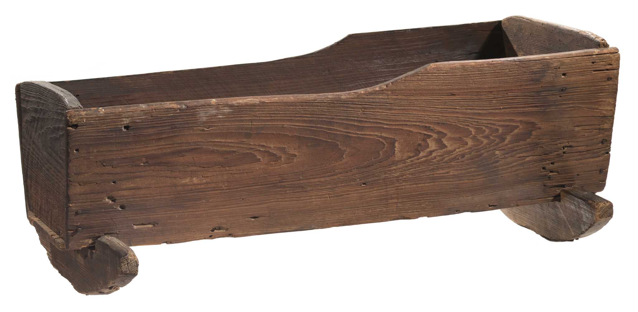 A wooden cradle made by an enslaved person consisting of 5 wooden boards nailed together to form a five-sided bed with open top on 2 rockers. The long sides are sloped, and the short sides have a rounded top edge.