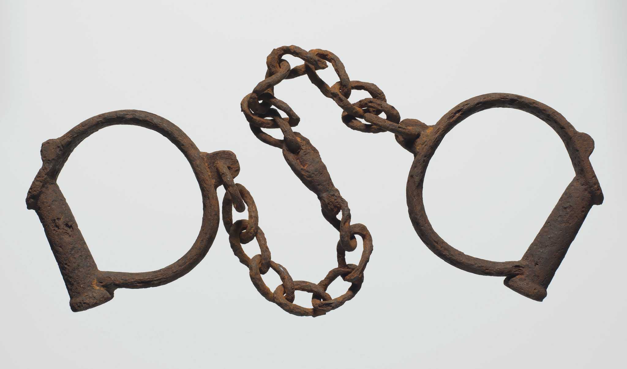 Two iron shackles consisting of iron loops joined together by a length of iron chain. The iron is heavily rusted.