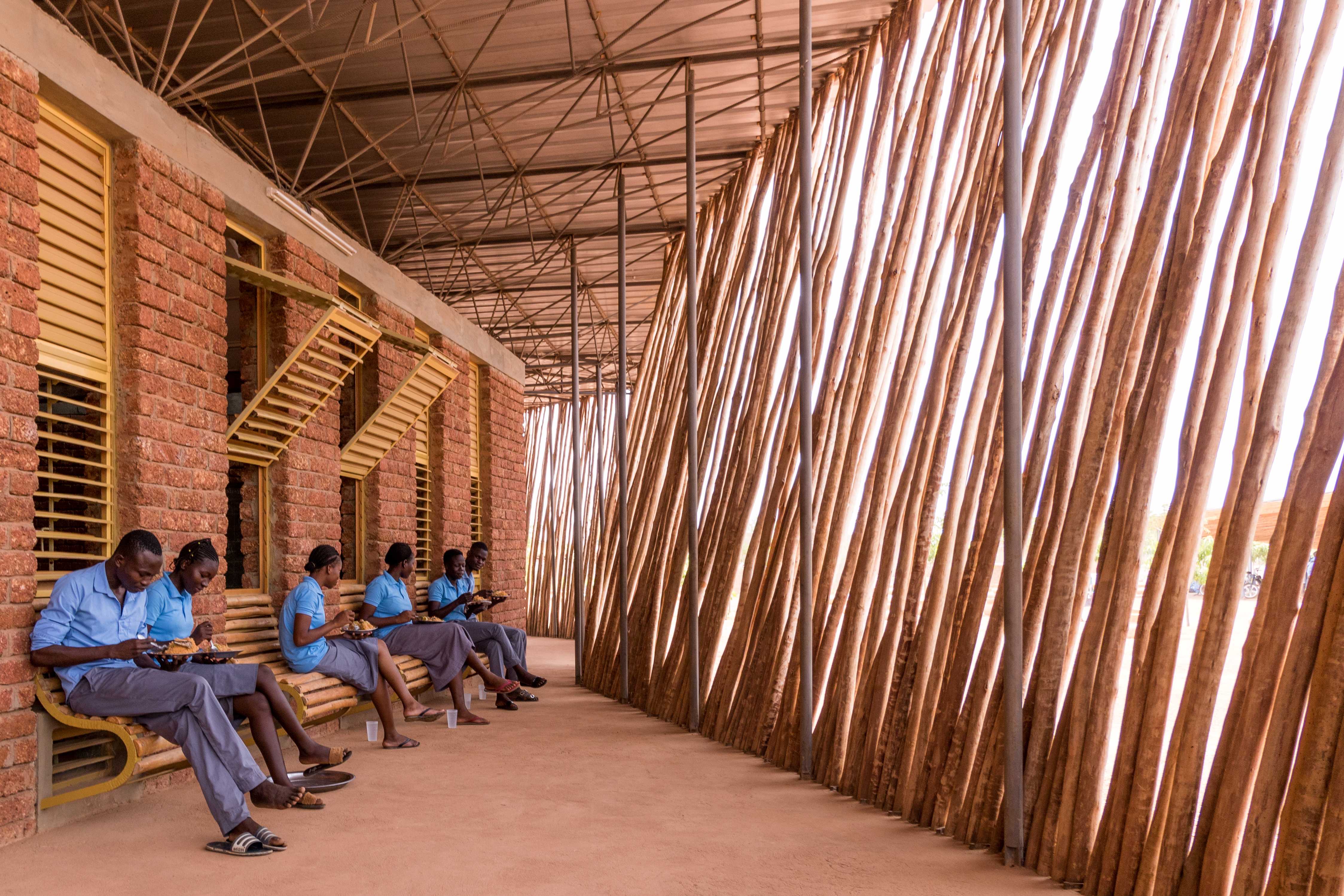 An inside view of the Lycée Schorge Secondary School with students sitting on wood benches and wooden divider.
