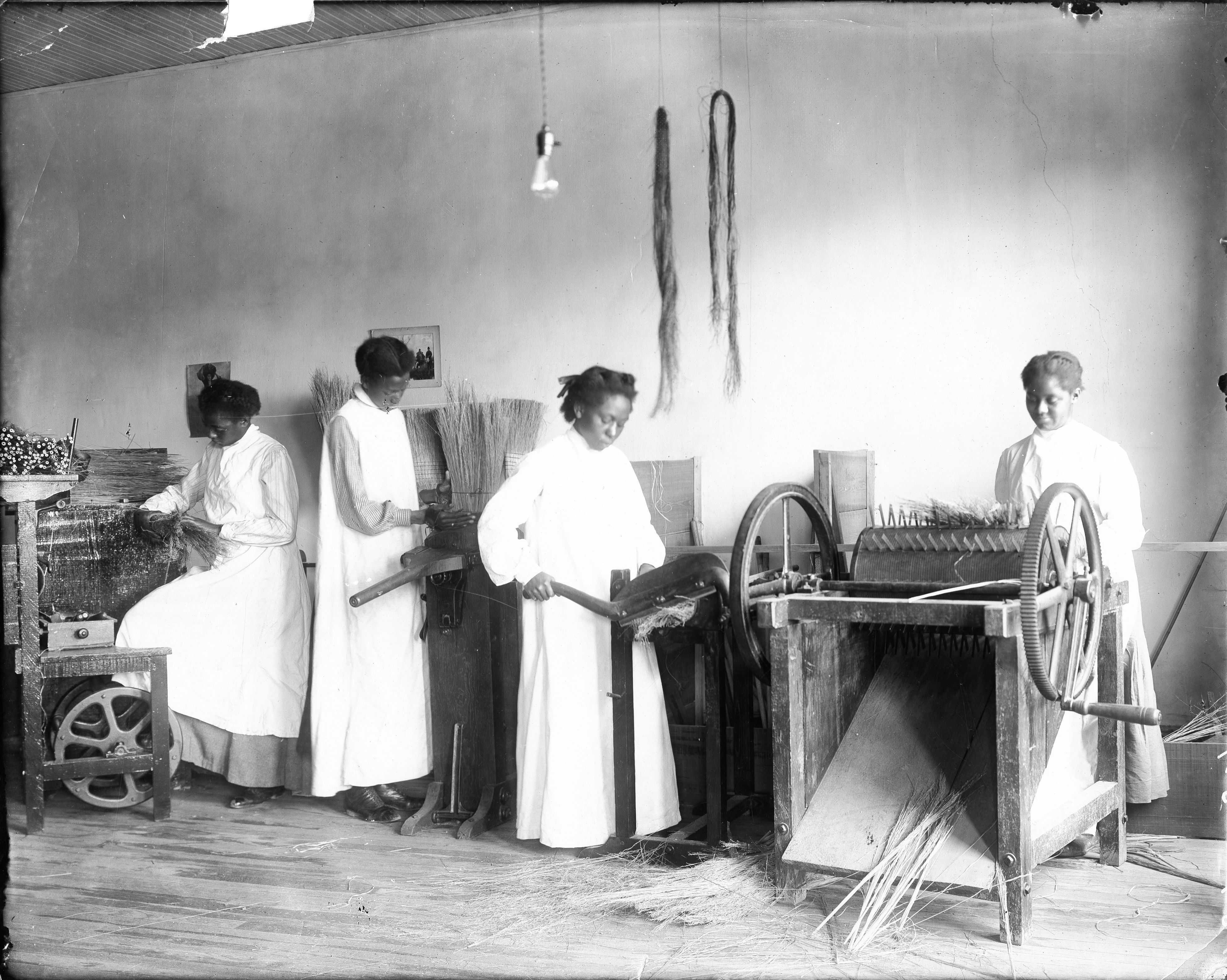 Black and white photograph of 4 female students making brooms, using machines.