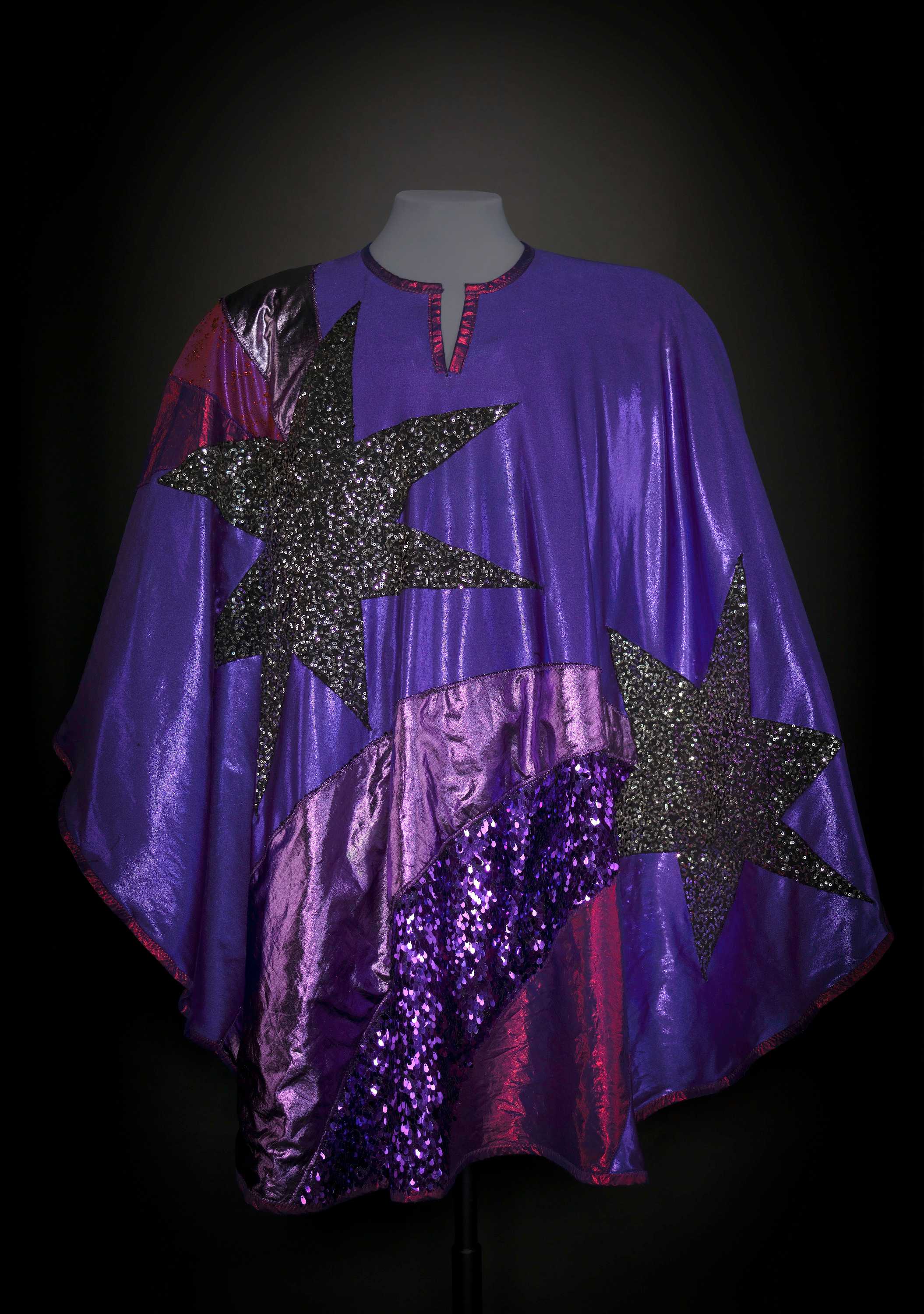 A purple poncho with different shades of purple and patterned strips and large sequences gray stars.