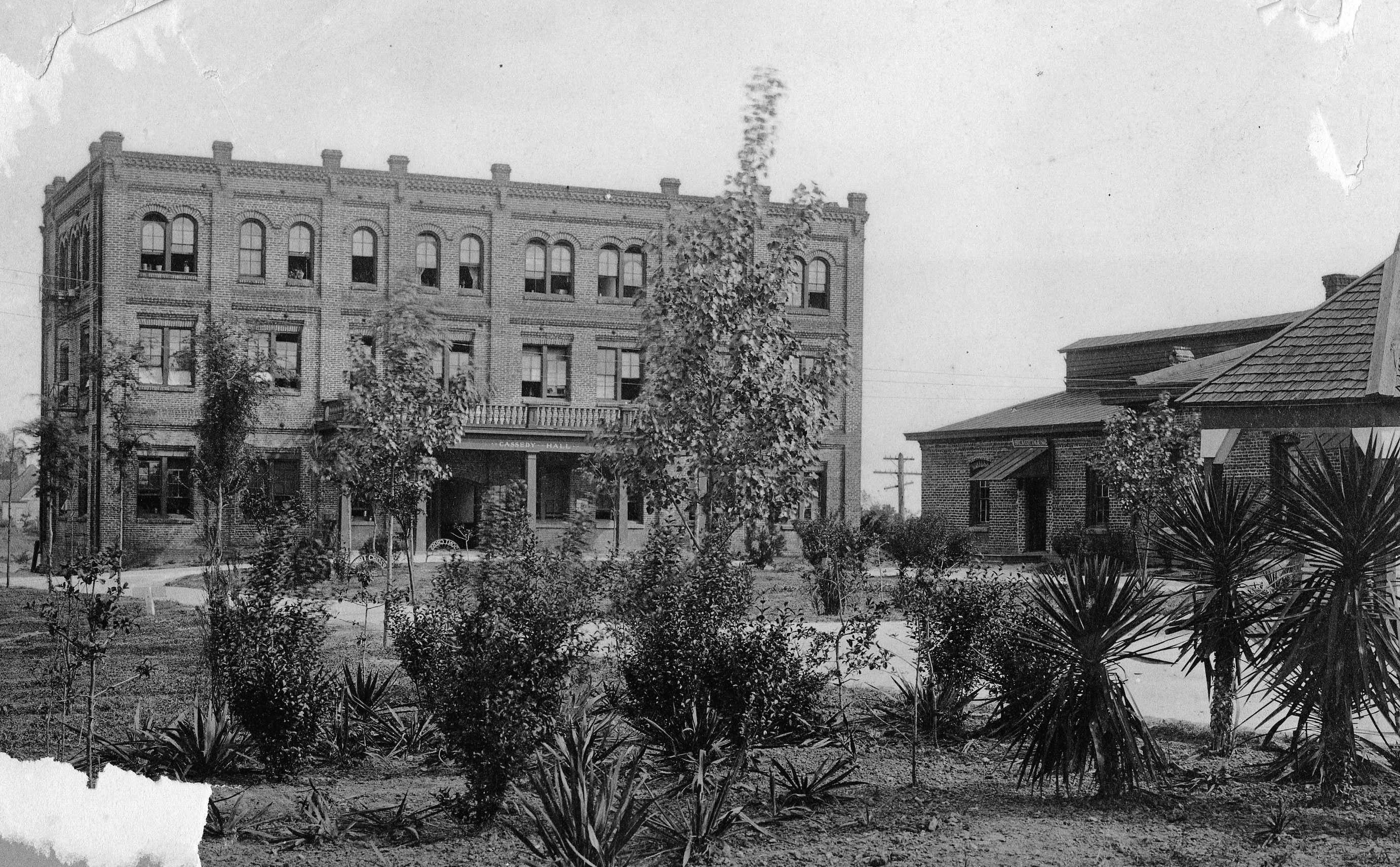 Photo of a three-story brick building with arched windows and a landscaped garden in the foreground.